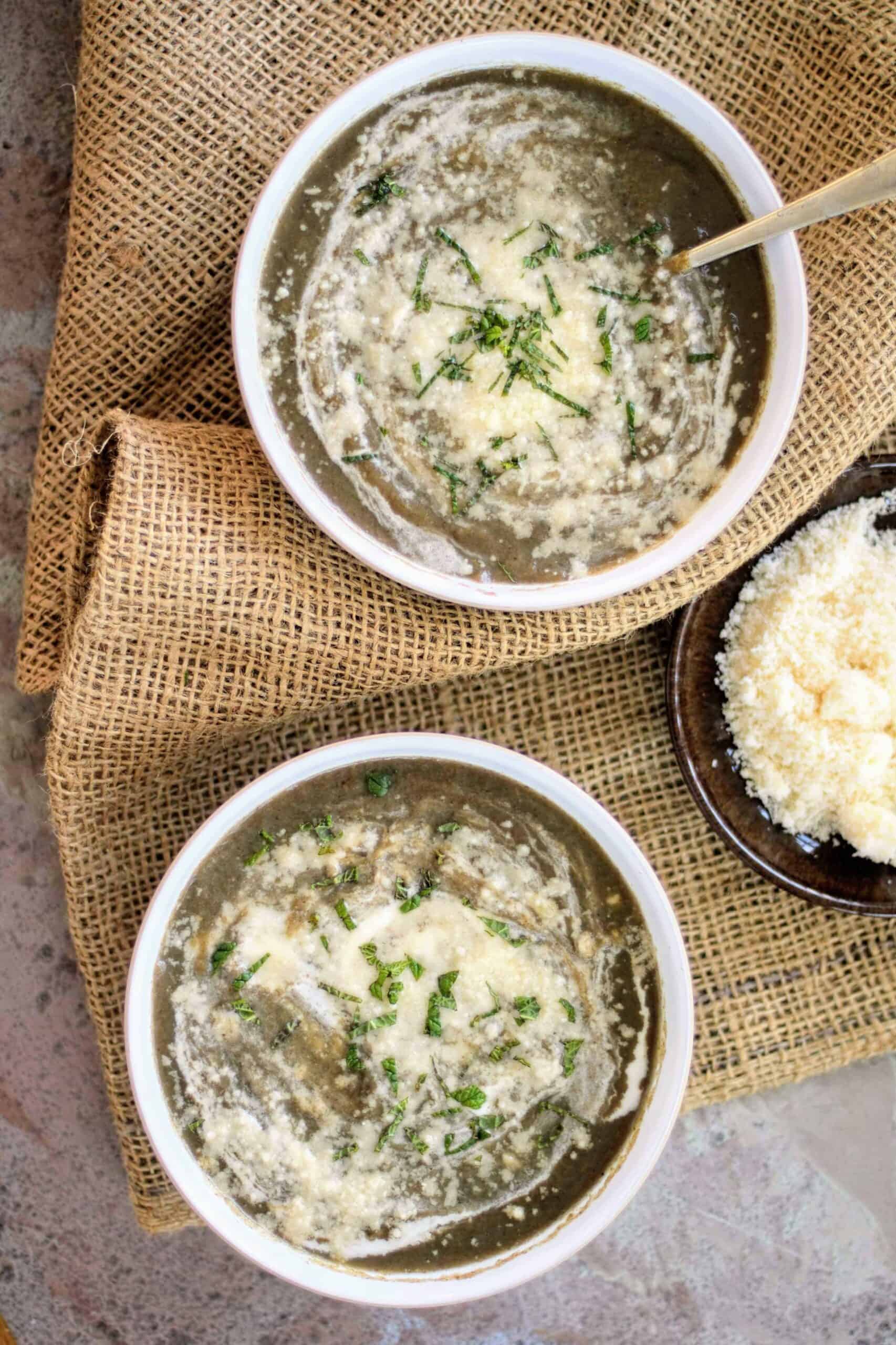 2 white bowls full of creamed mushroom soup with cheese and herbs placed on a hessian sack