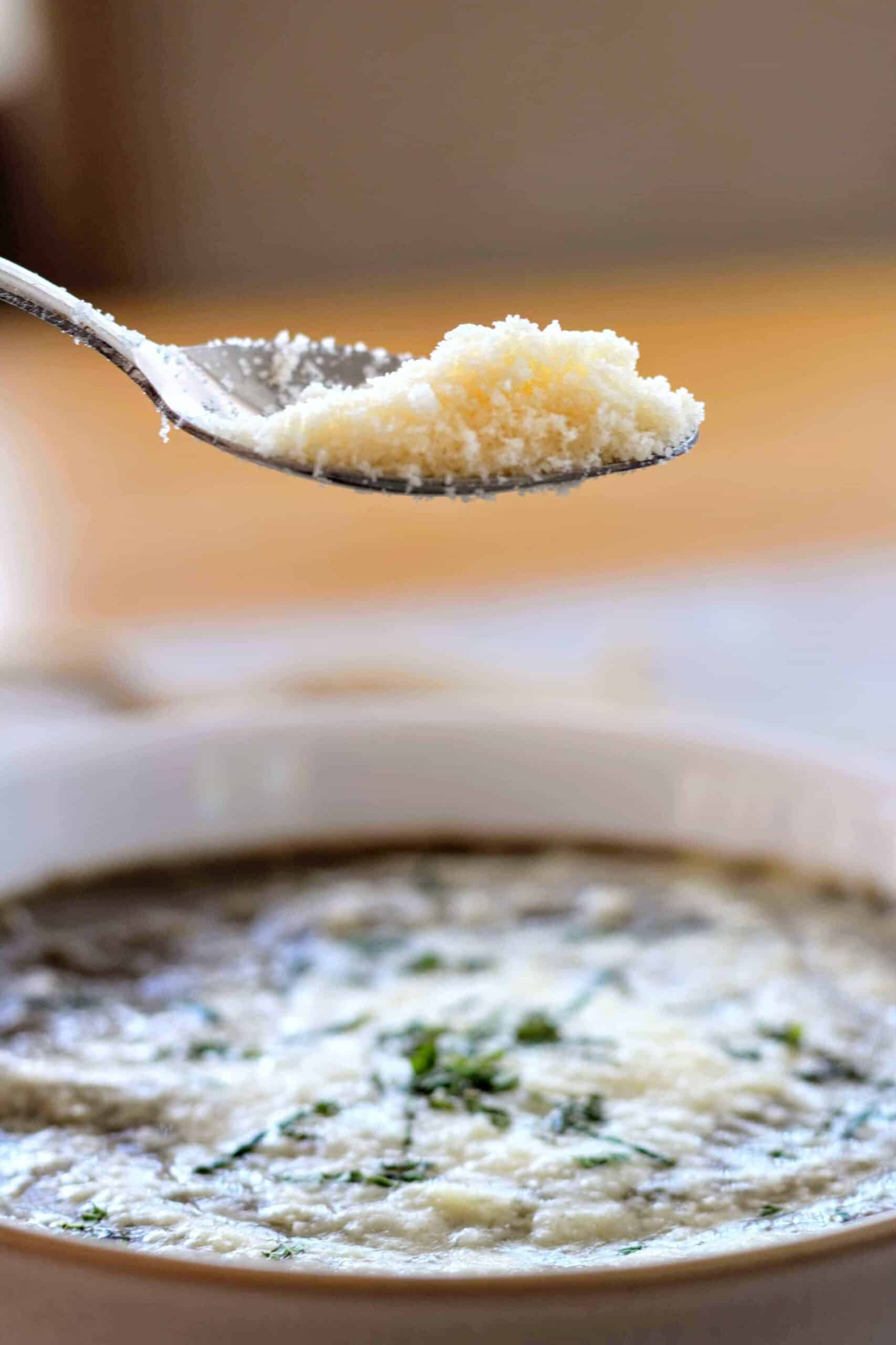 person sprinkling grated Parmesan on top of mushroom soup