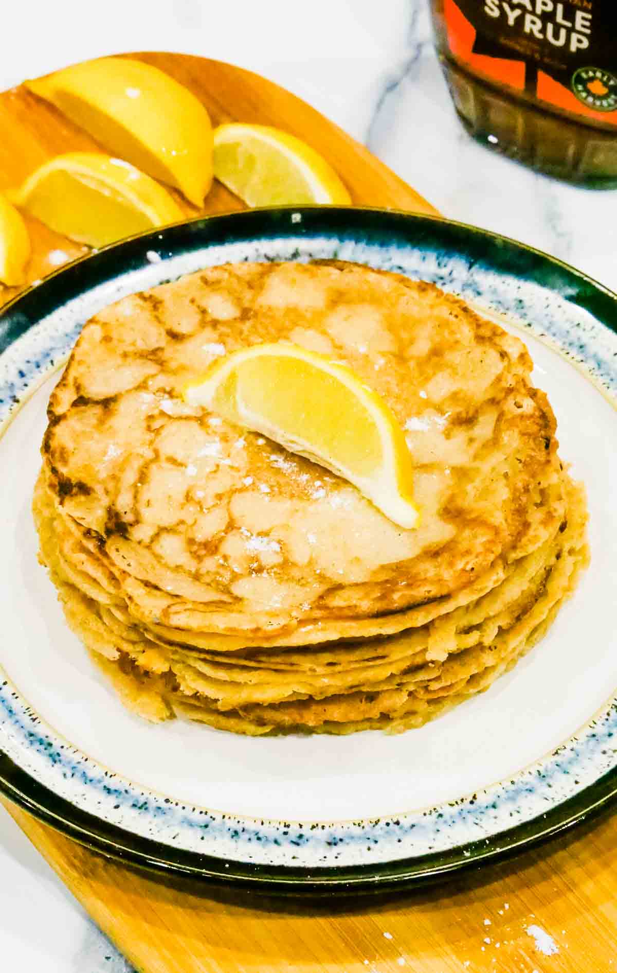 stack of vegan pancakes on a plate with lemon slices and maple syrup