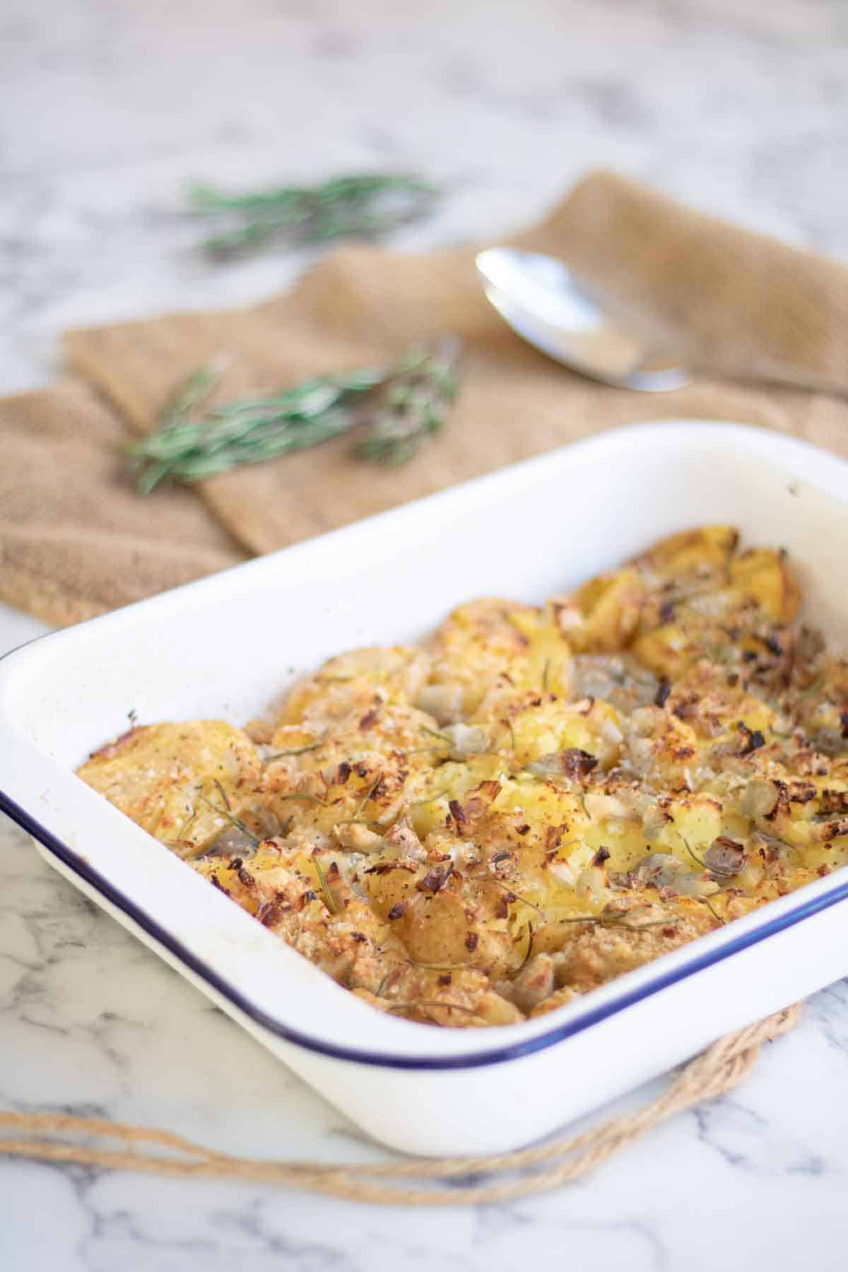 White enamel roasting tin full of unofficial Slimming World crushed new potatoes on white marble kitchen countertop
