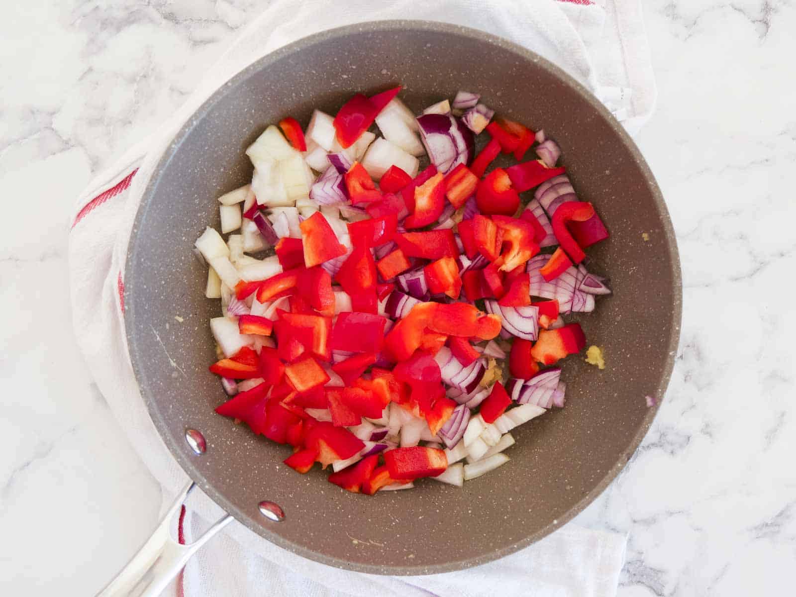 Large frying pan full of fresh onions, peppers, ginger and garlic.