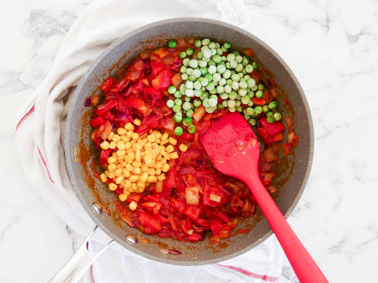Fried vegetables in a large frying pan with added sweetcorn and frozen peas