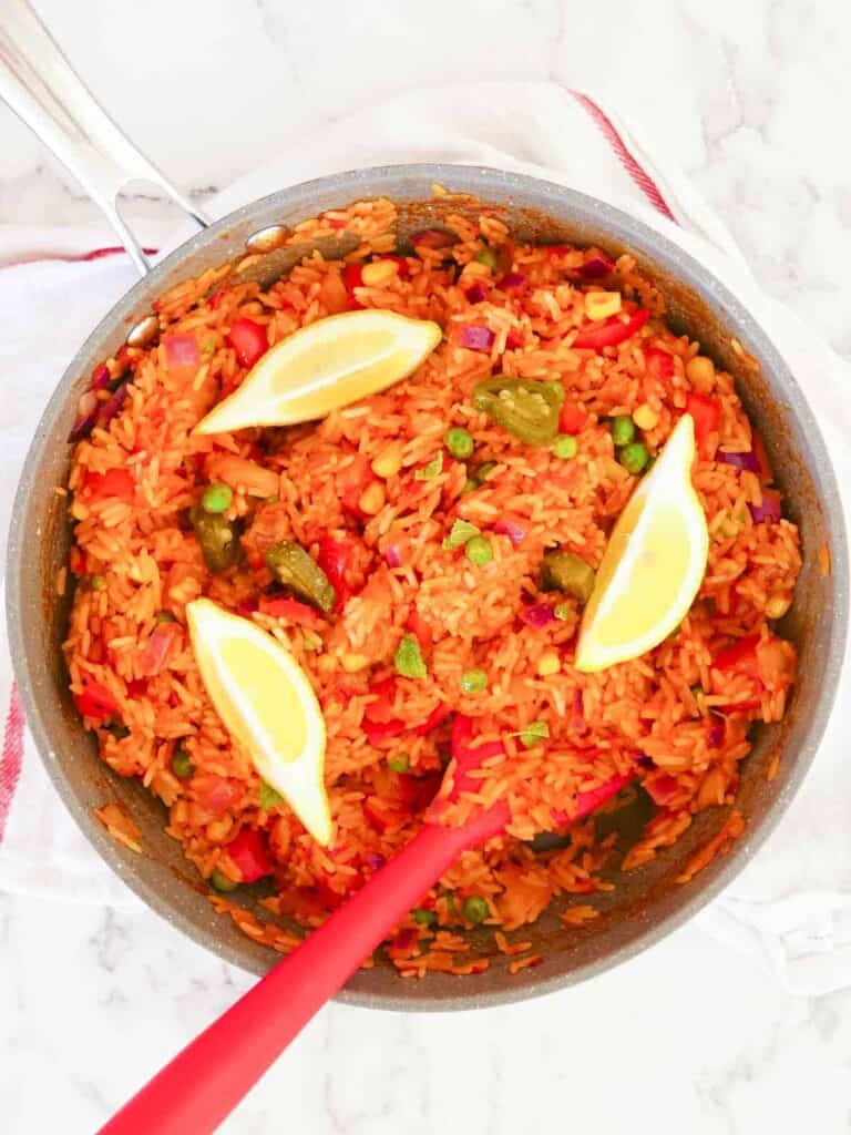 Large Stellar pan full of Mexican fried rice with a red spatula and 3 lemon wedges and lemon balm