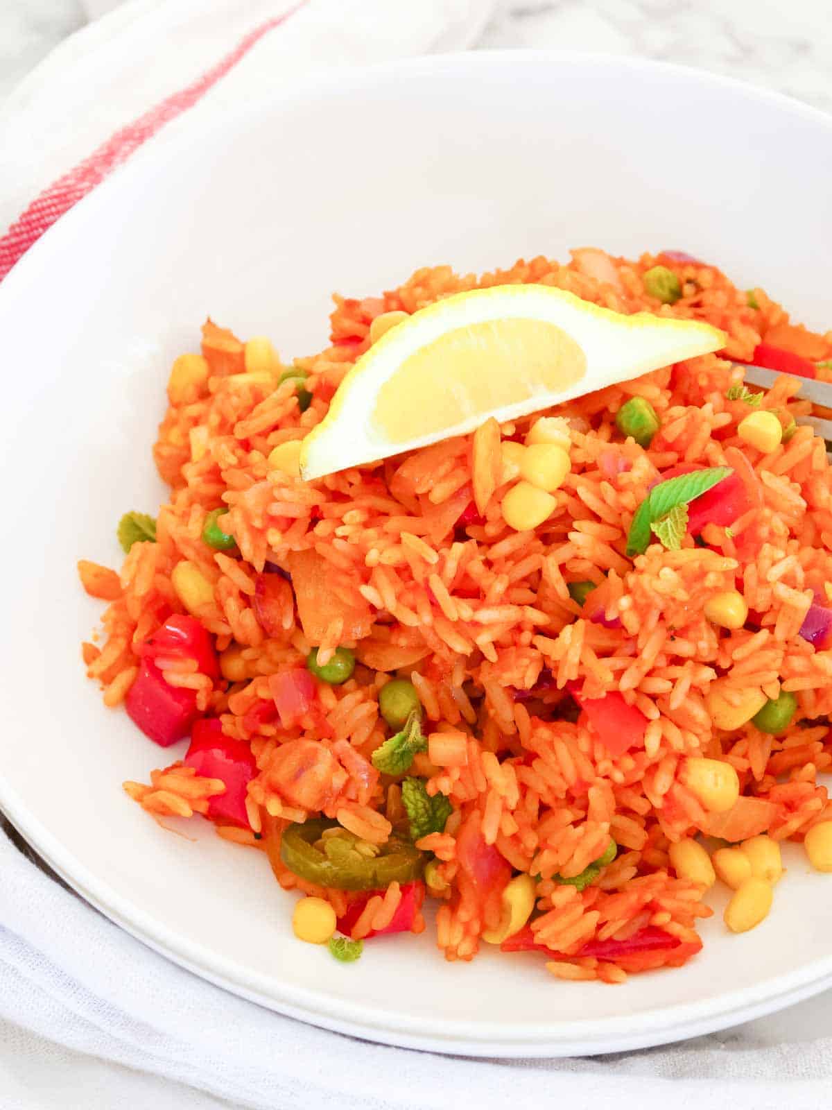 Close up of a spicy vegetable fried rice with lemon wedge in a white Denby bowl.