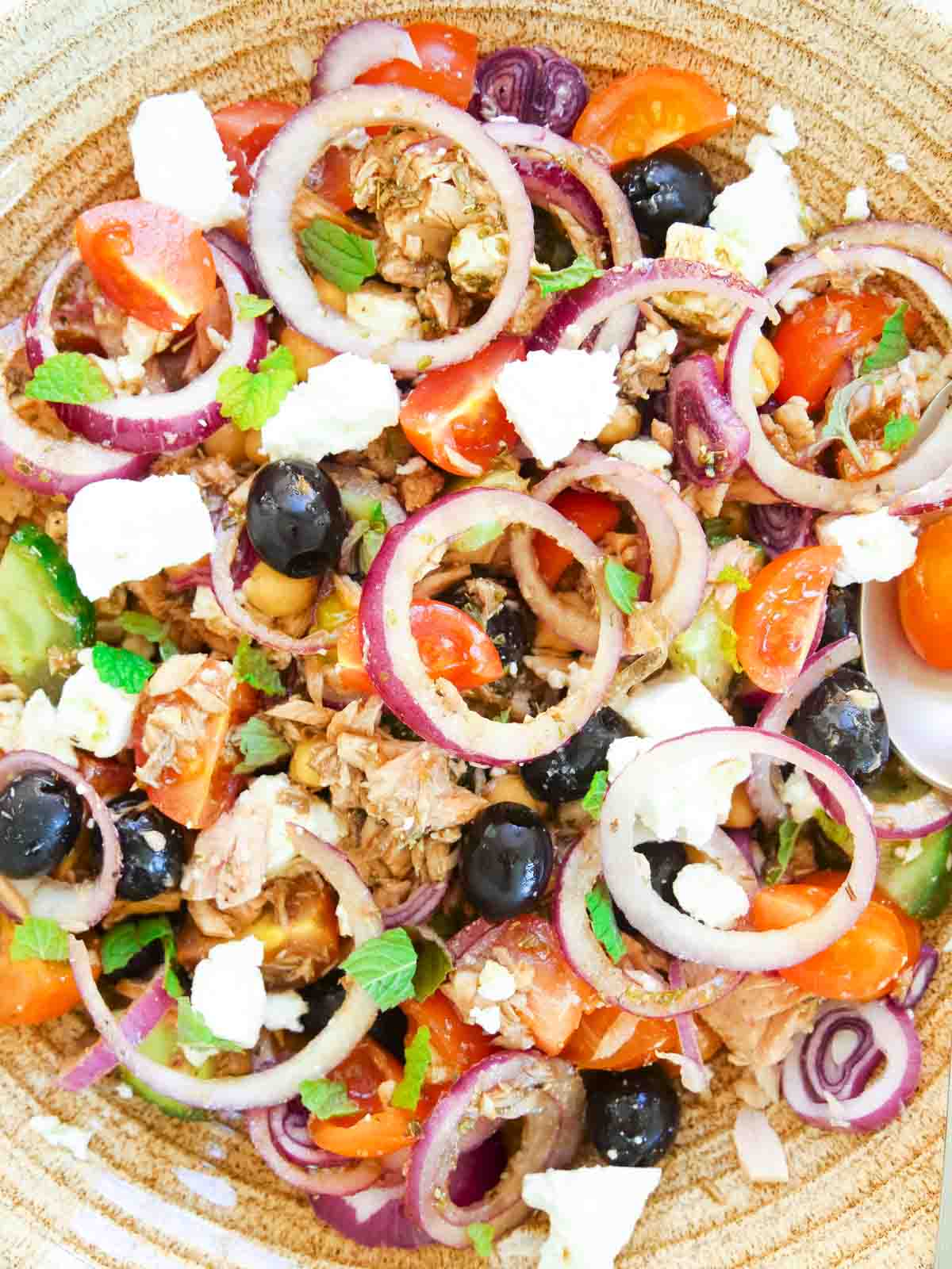 Salad full of Sliced red onion rings, olives, tuna, extra virgin olive oil mixed in a large Denby bowl