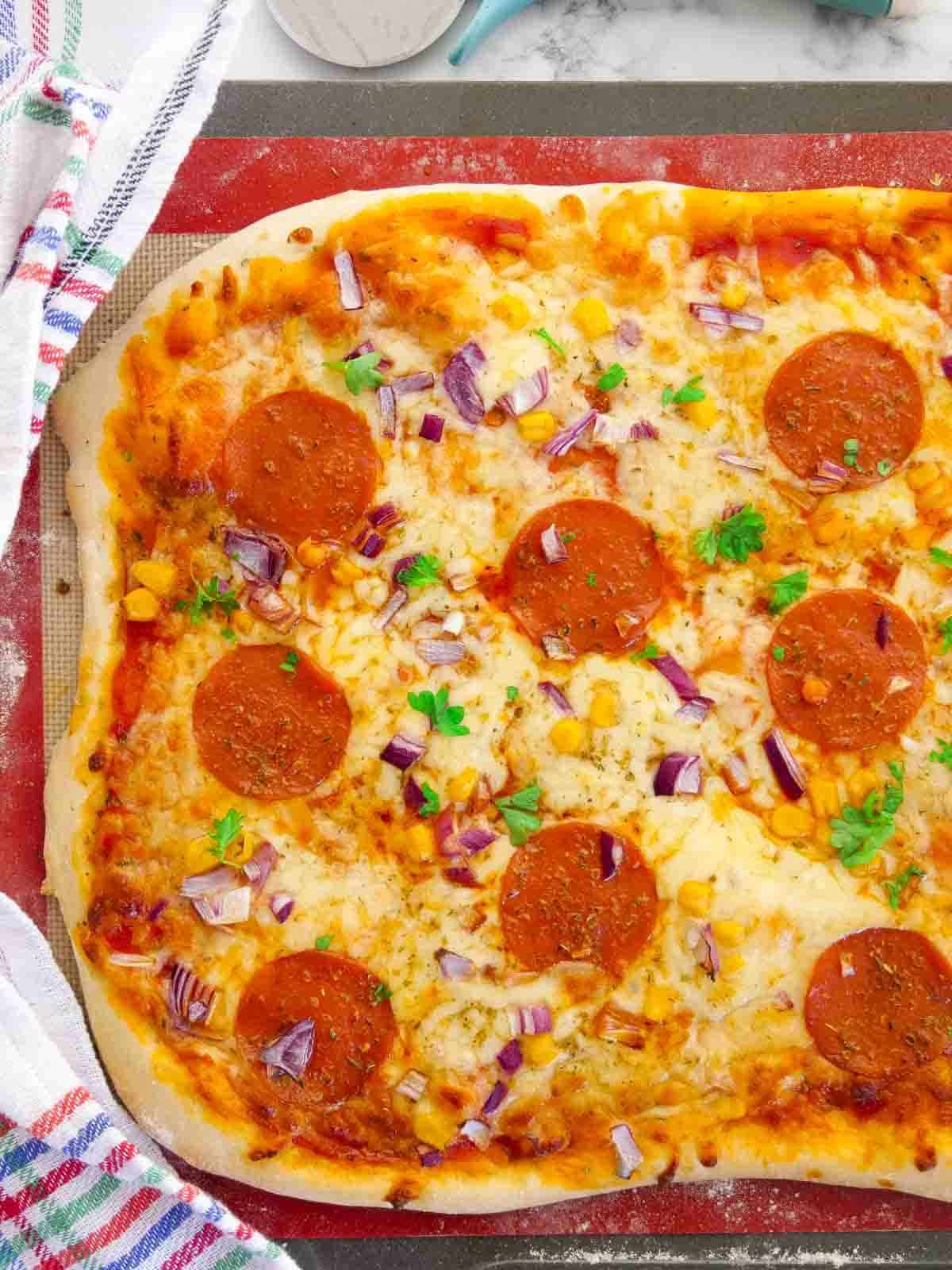 Close up of a pepperoni pizza a silicone mat lined baking tray on marble kitchen counter