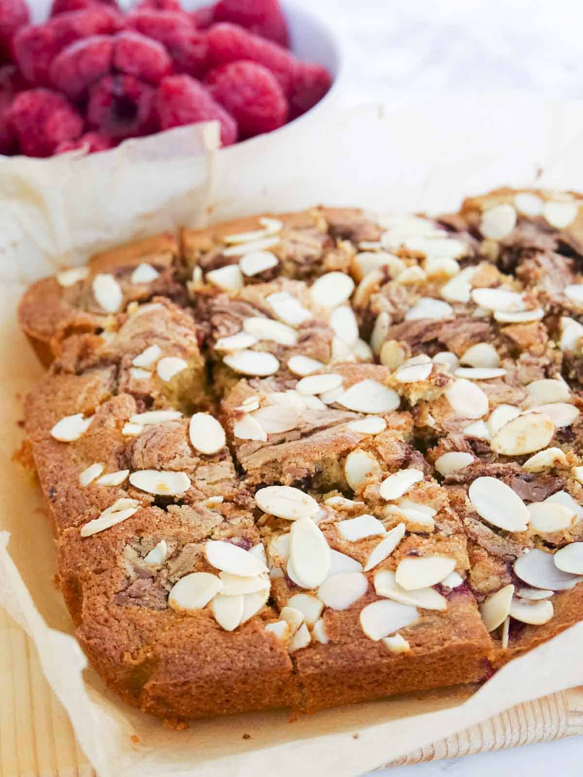 Sliced up baked raspberry cake with chocolate and almonds on a wooden serving platter