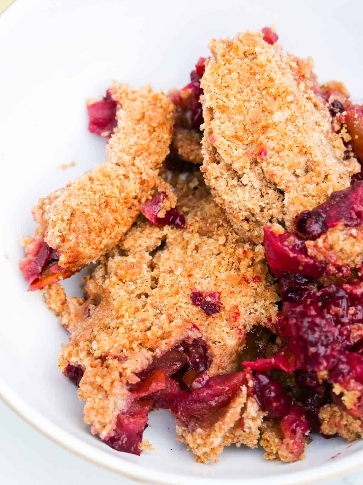 close up of fruity apple and berry crumble in a white bowl