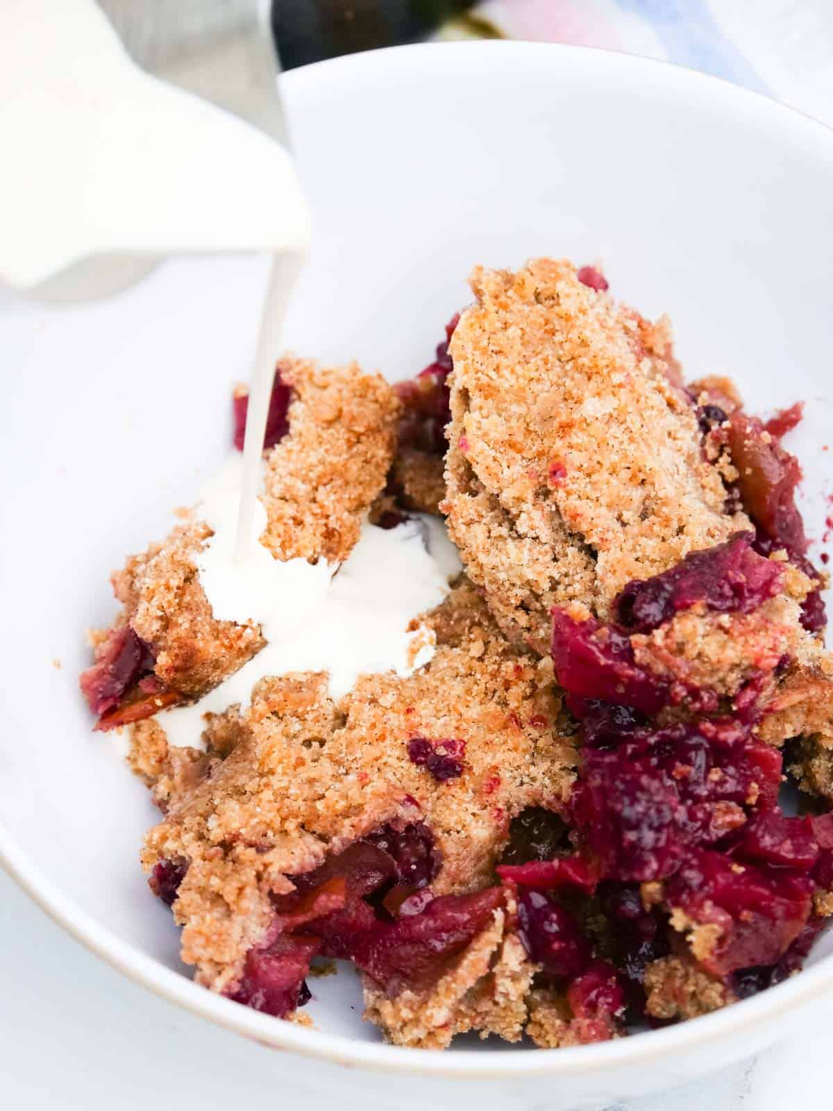 pouring vegan plant based double cream on apple and blackberry crumble