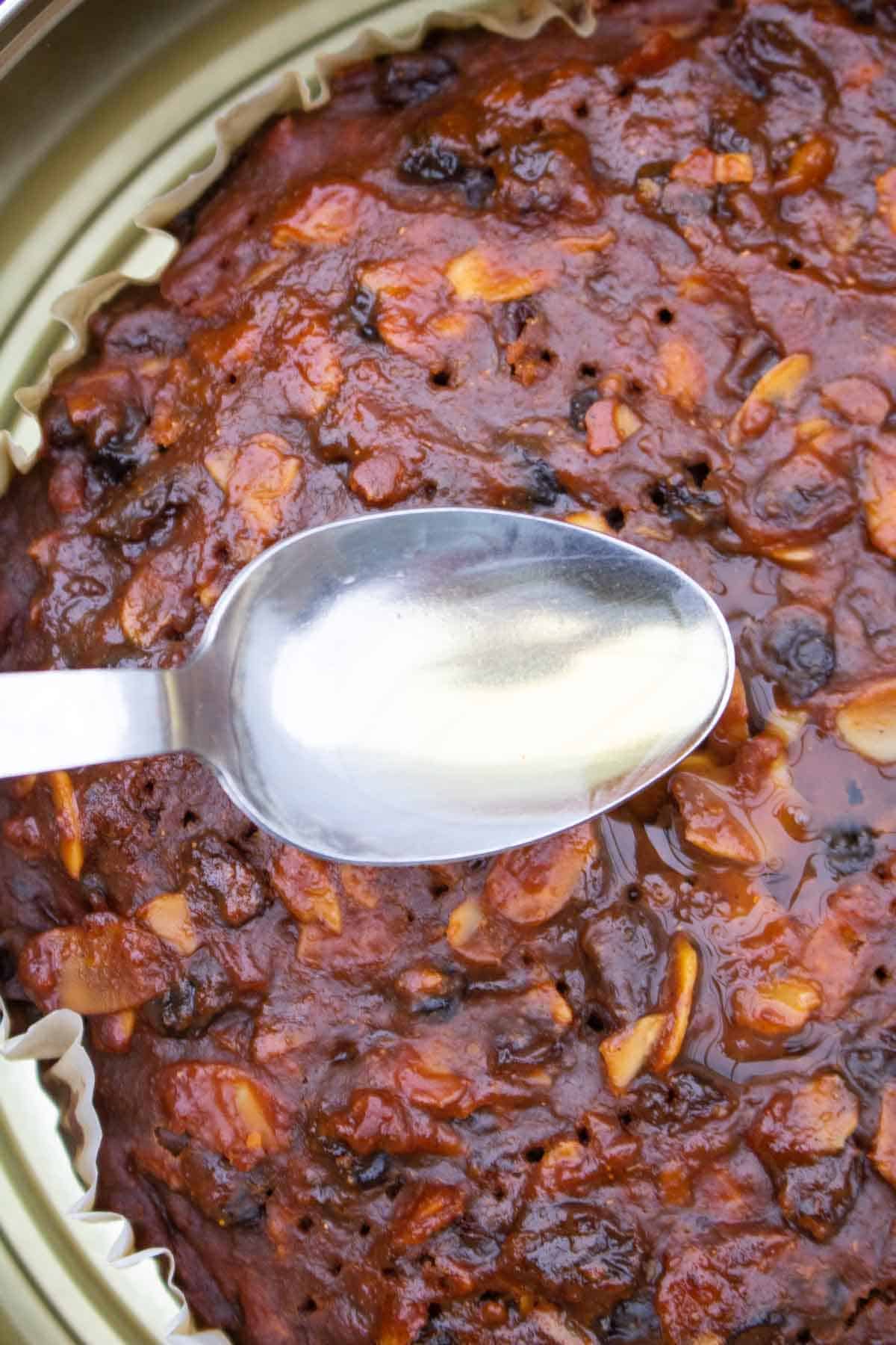 Spooning over French brandy into fork pricked holes in a Christmas cake