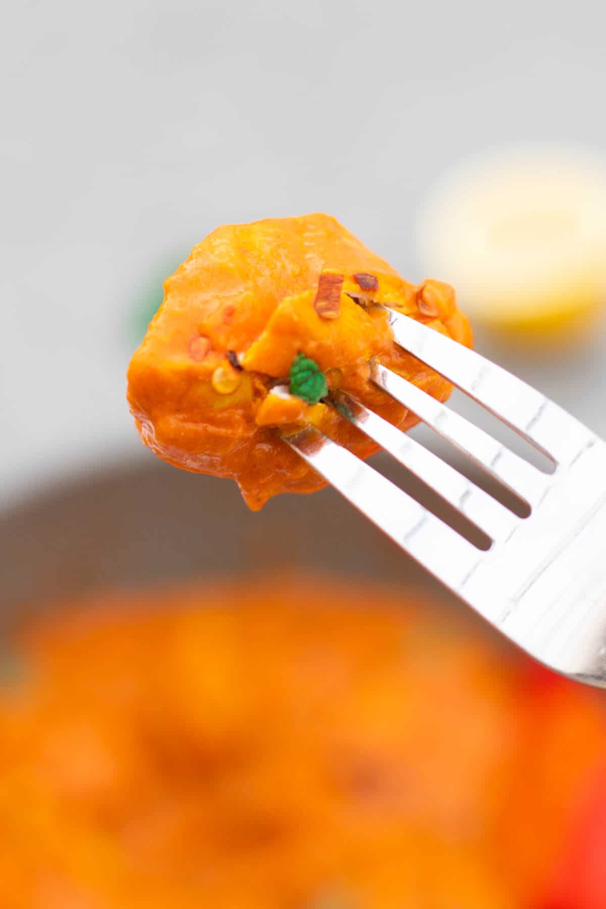Fork with a chicken chunk in a curry creamy tomato curry sauce