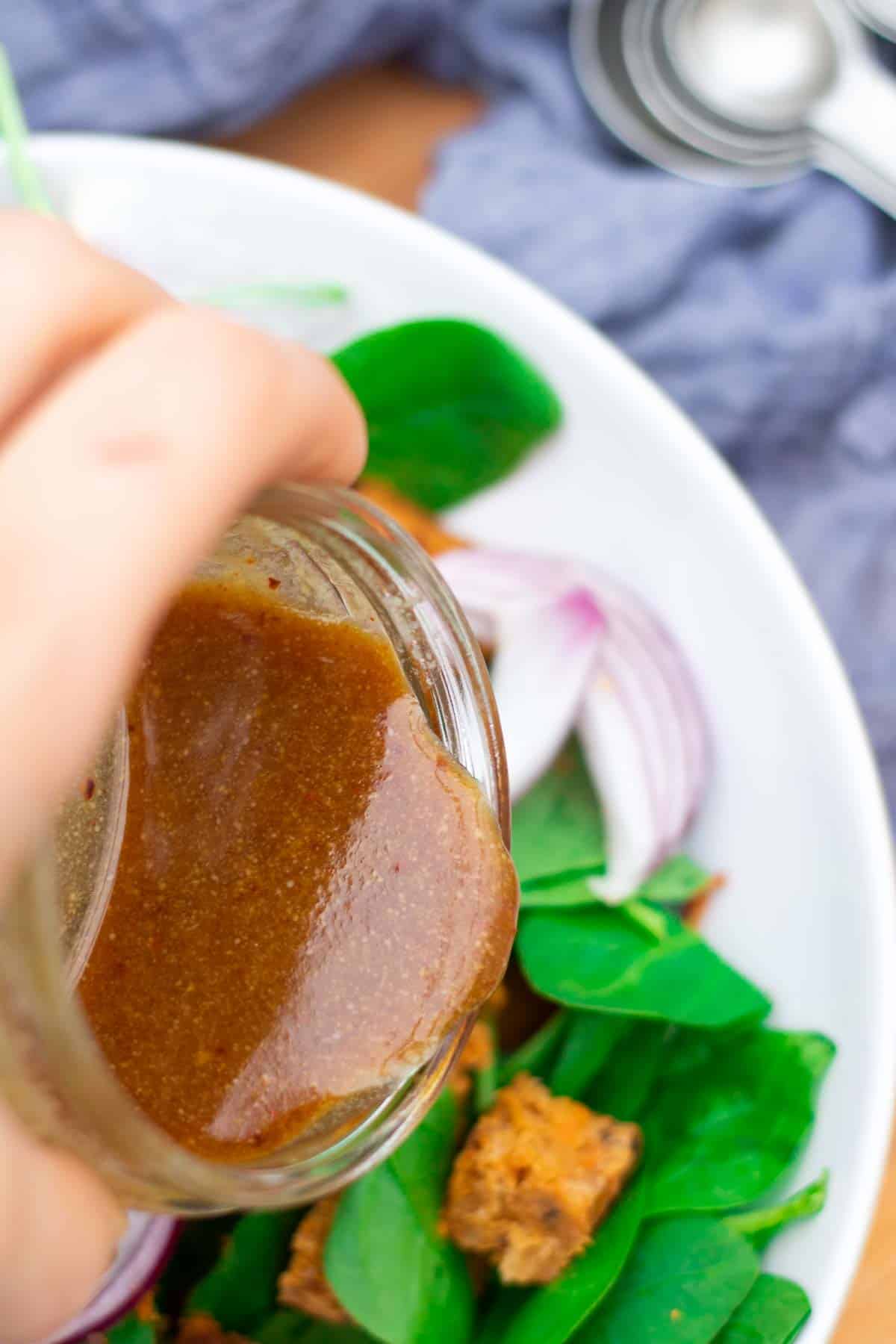 Close up of a quick recipe for tahini dressing being poured over a vegan salad