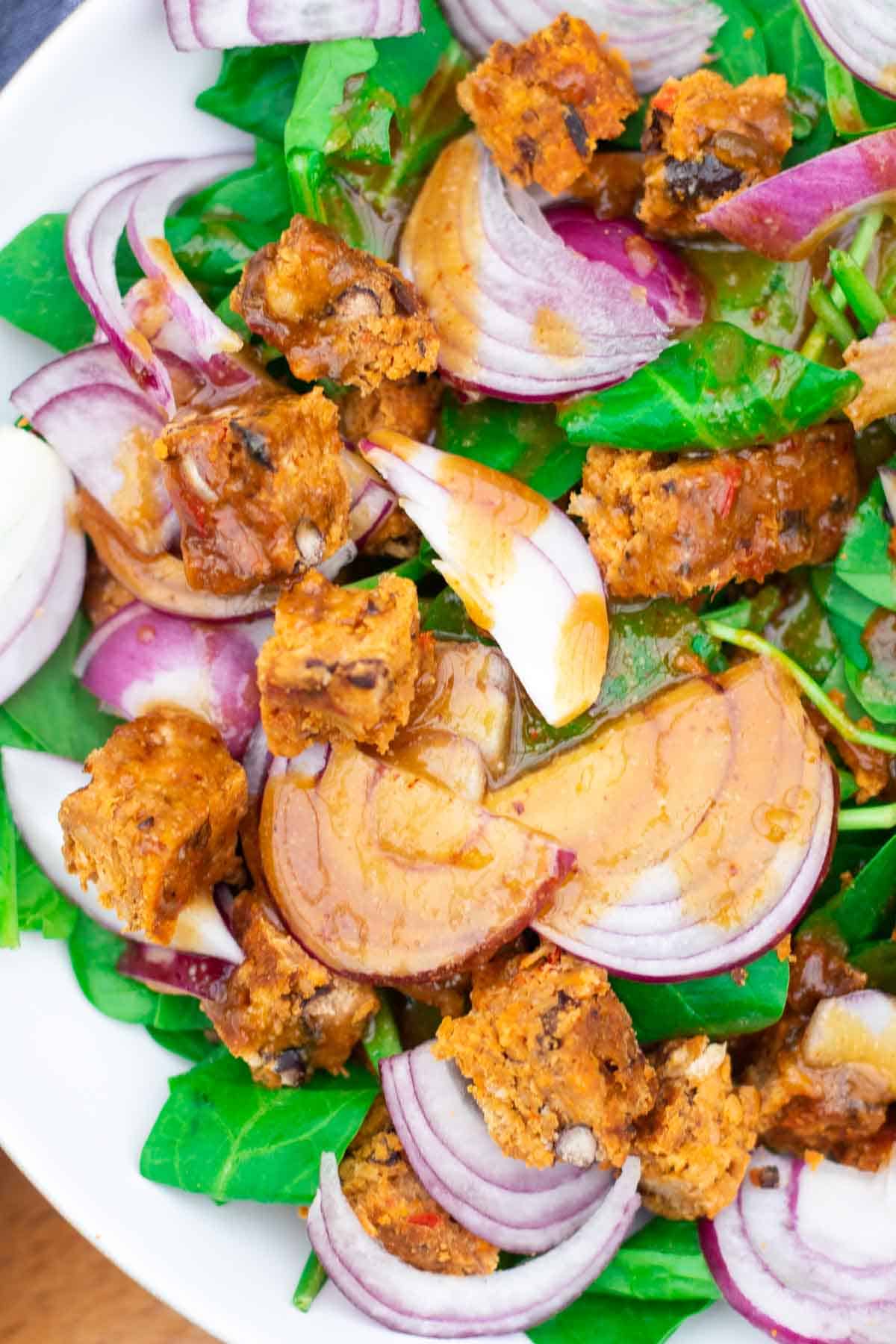 Close up of a delicious tahini salad recipe full of red onions, vegan bean burgers and spinach