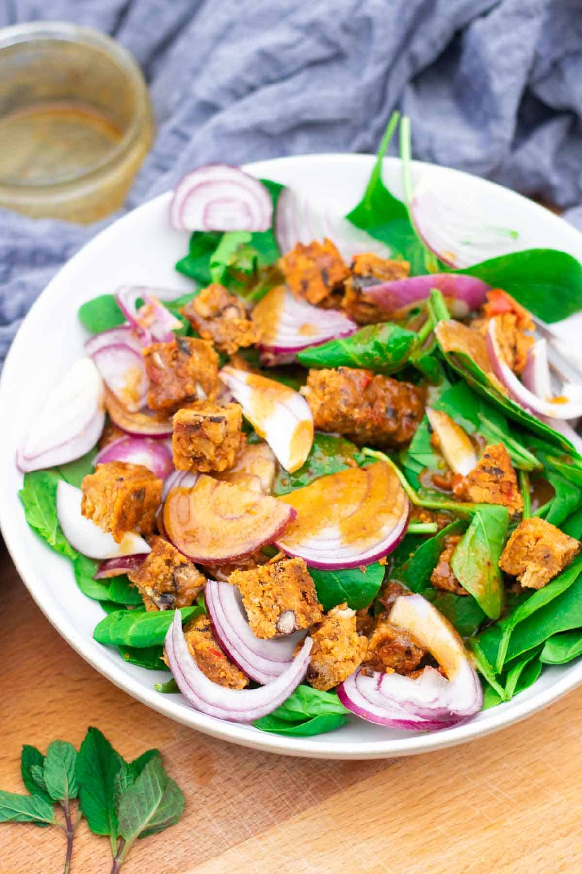 Maple syrup and tahini dressing drizzled on top of a vegan bean burger and spinach with red onion salad in a white bowl