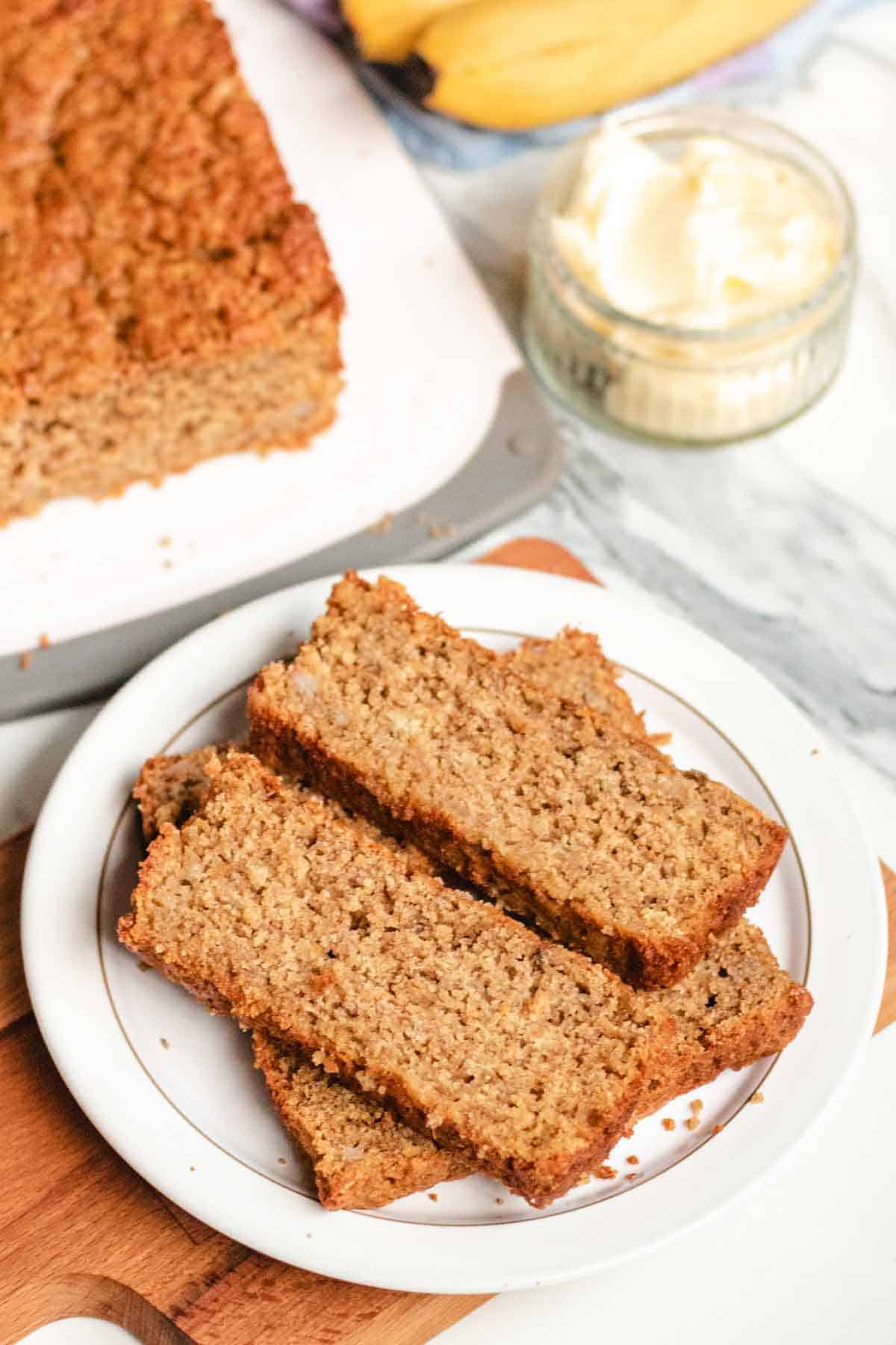 Slices of banana cake on a white Denby plate on wooden chopping board