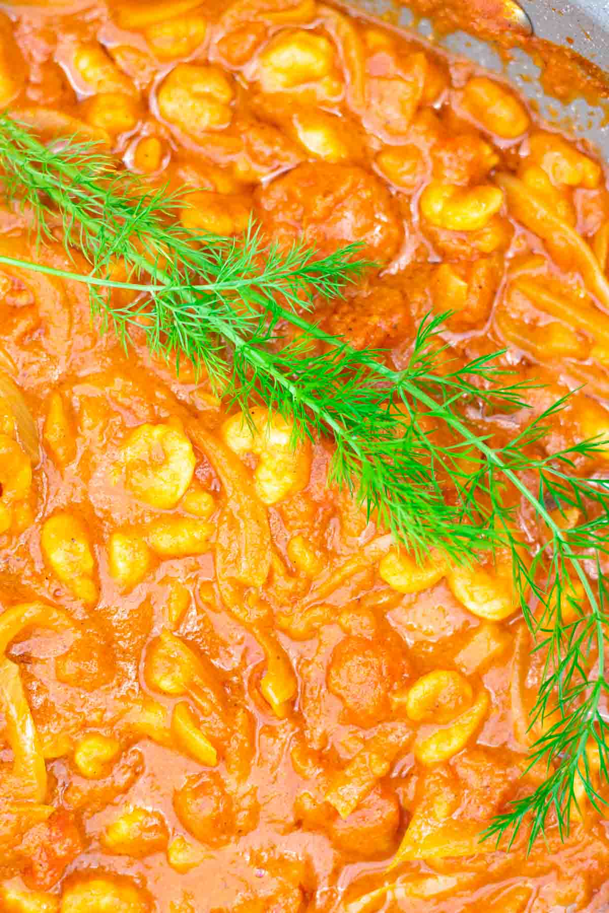 Close up of precooked prawns in a bhuna Indian curry sauce garnished with fresh fennel