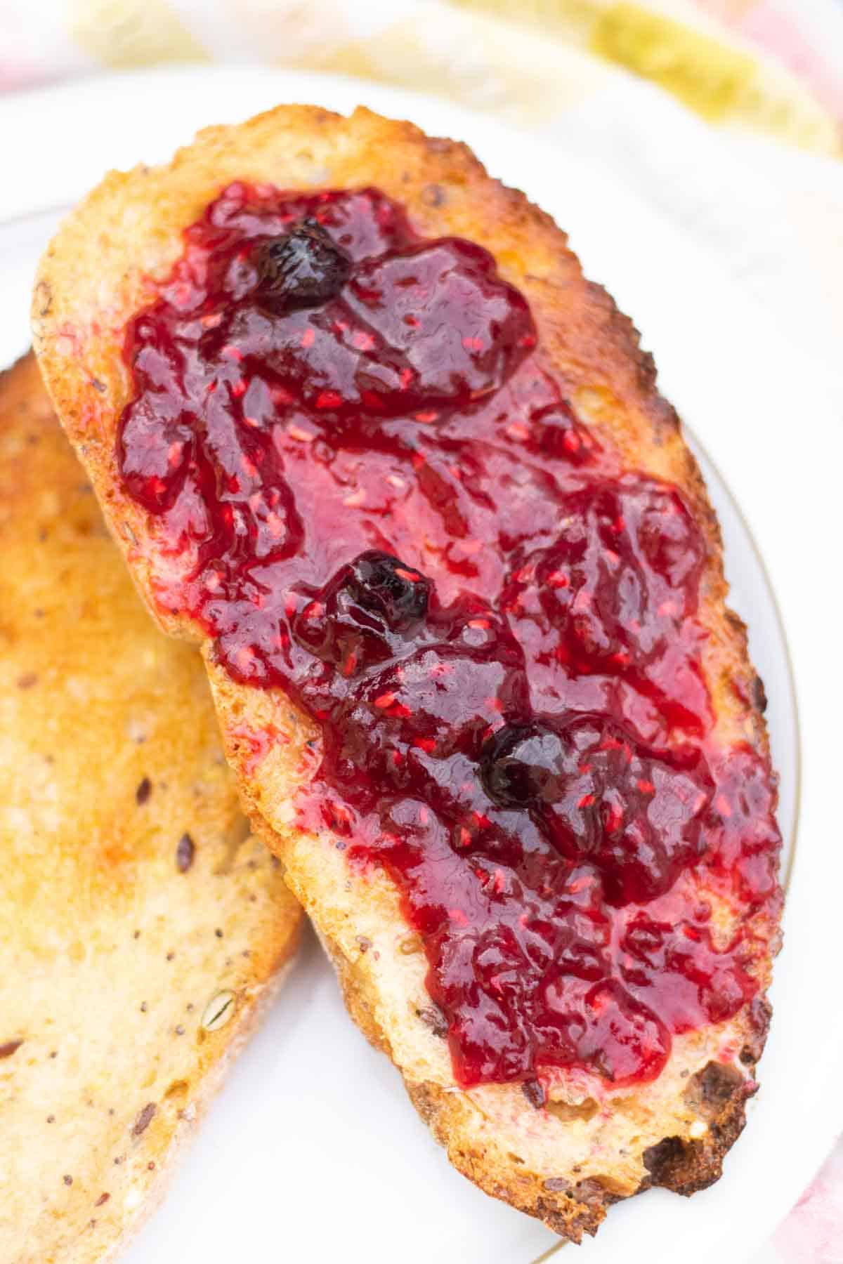 Close up of raspberry jam with blueberries spread on sourdough toast