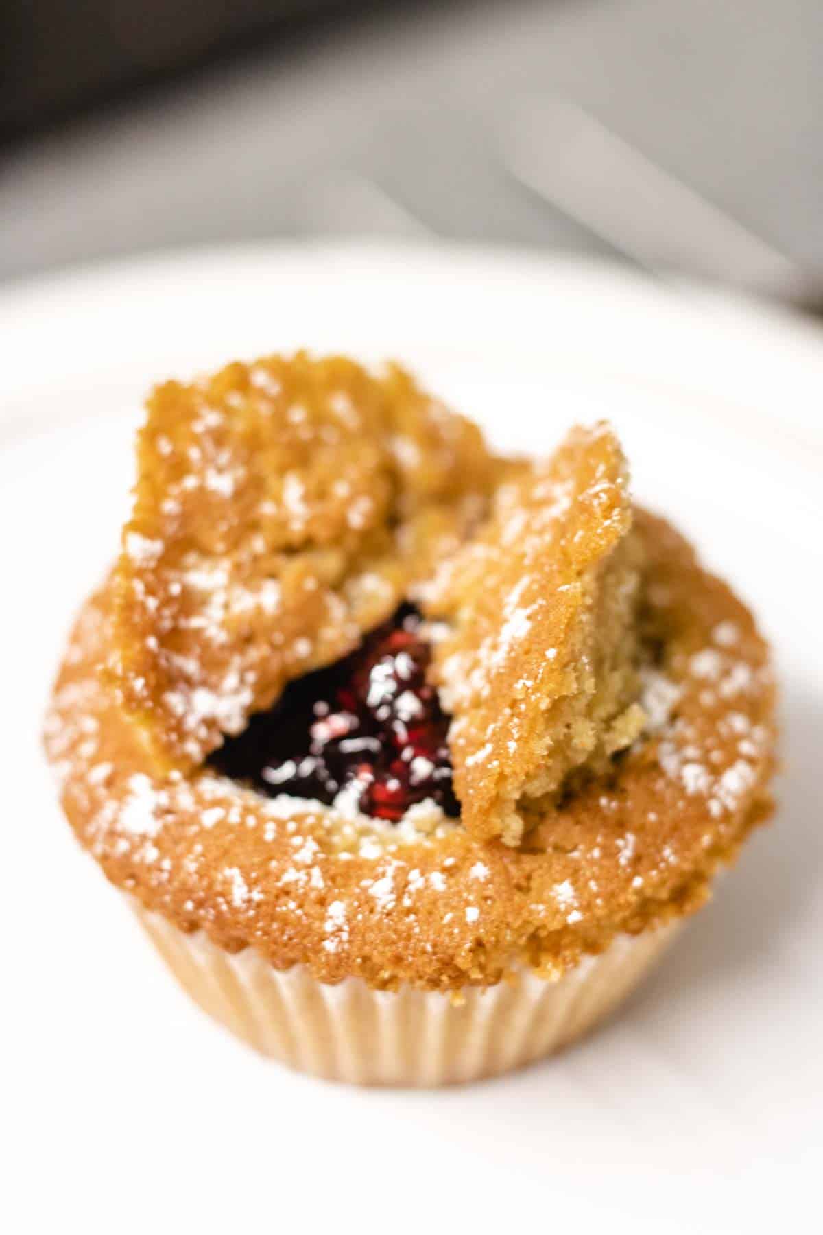 Close up of a golden easy butterfly cupcake filled with Queens jam and dusted with icing sugar on white plate
