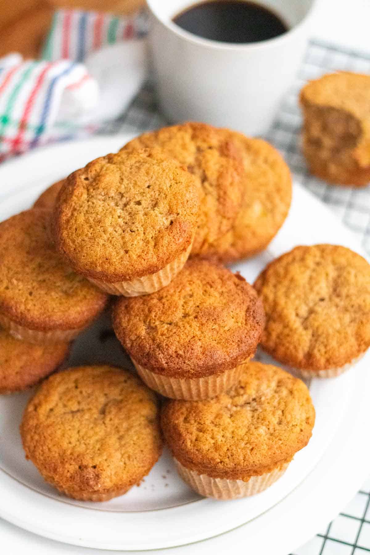 Pile of golden banana muffins on a white plate alongside a cup of coffee