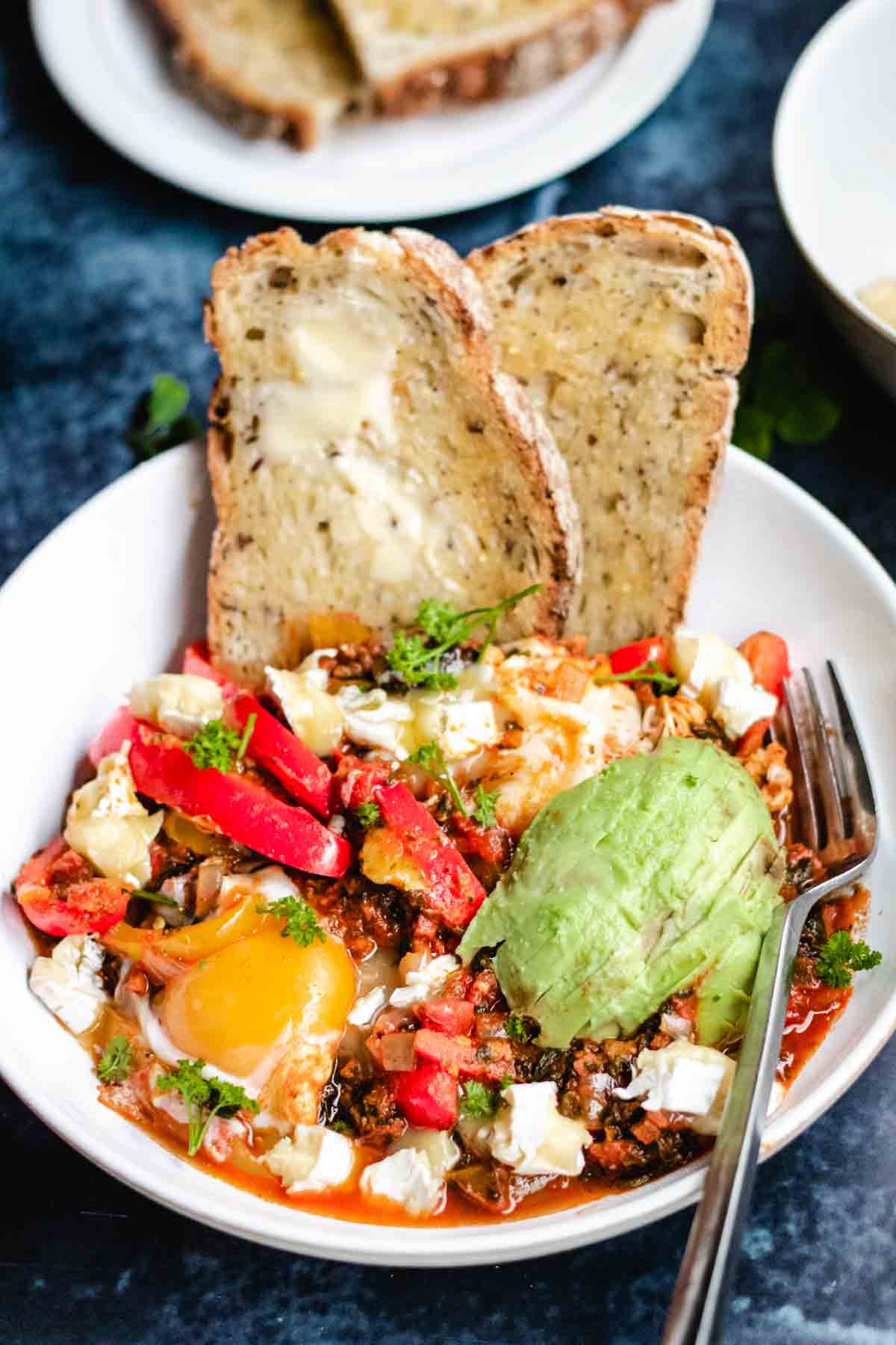 Close up of baked eggs in tomatoes with red pepper and buttered sourdough toast.