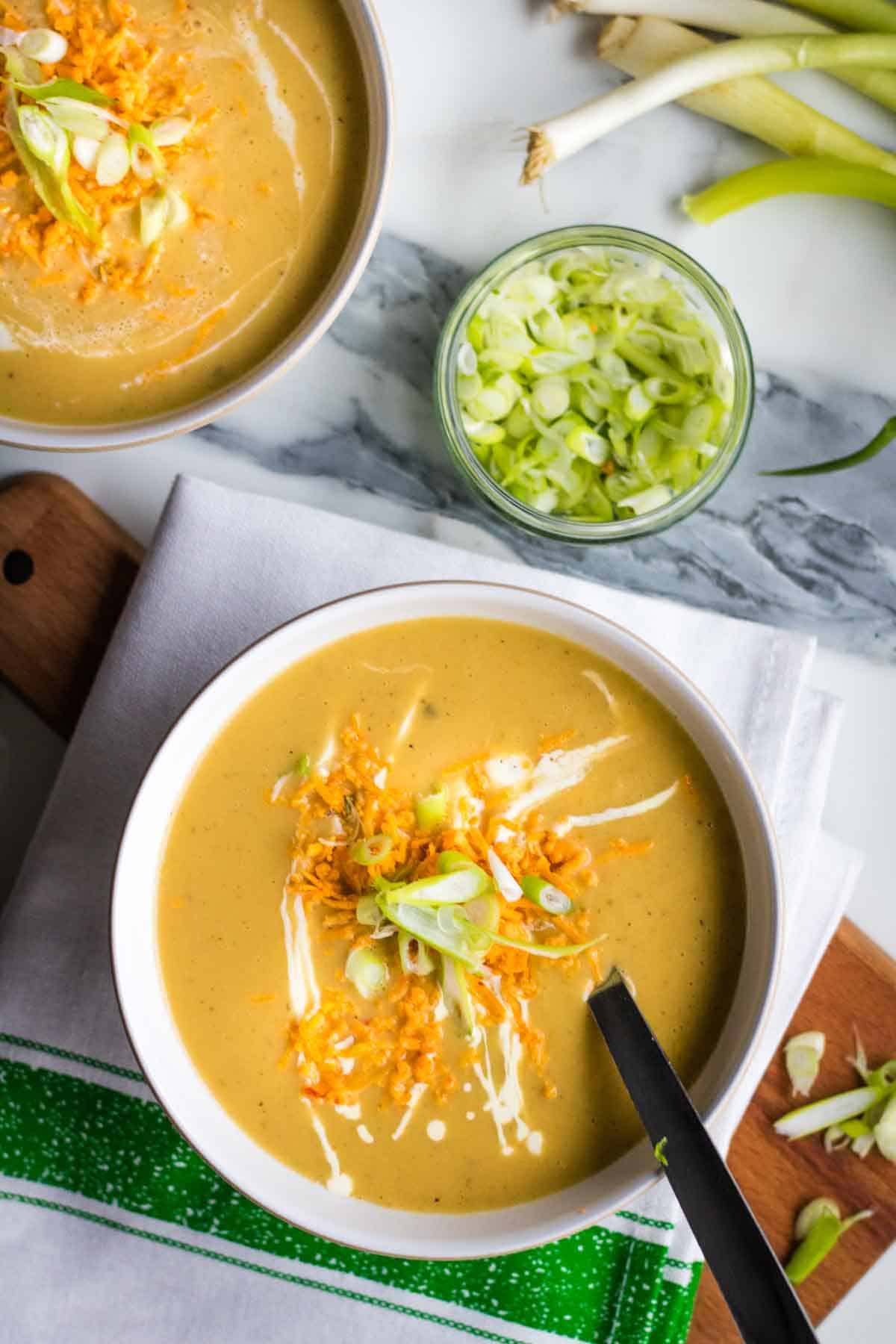 cheese and spring onion soup in a white bowl with bowl of spring onions