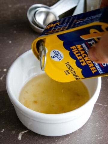 person draining oil from canned mackerel into a ramekin dish