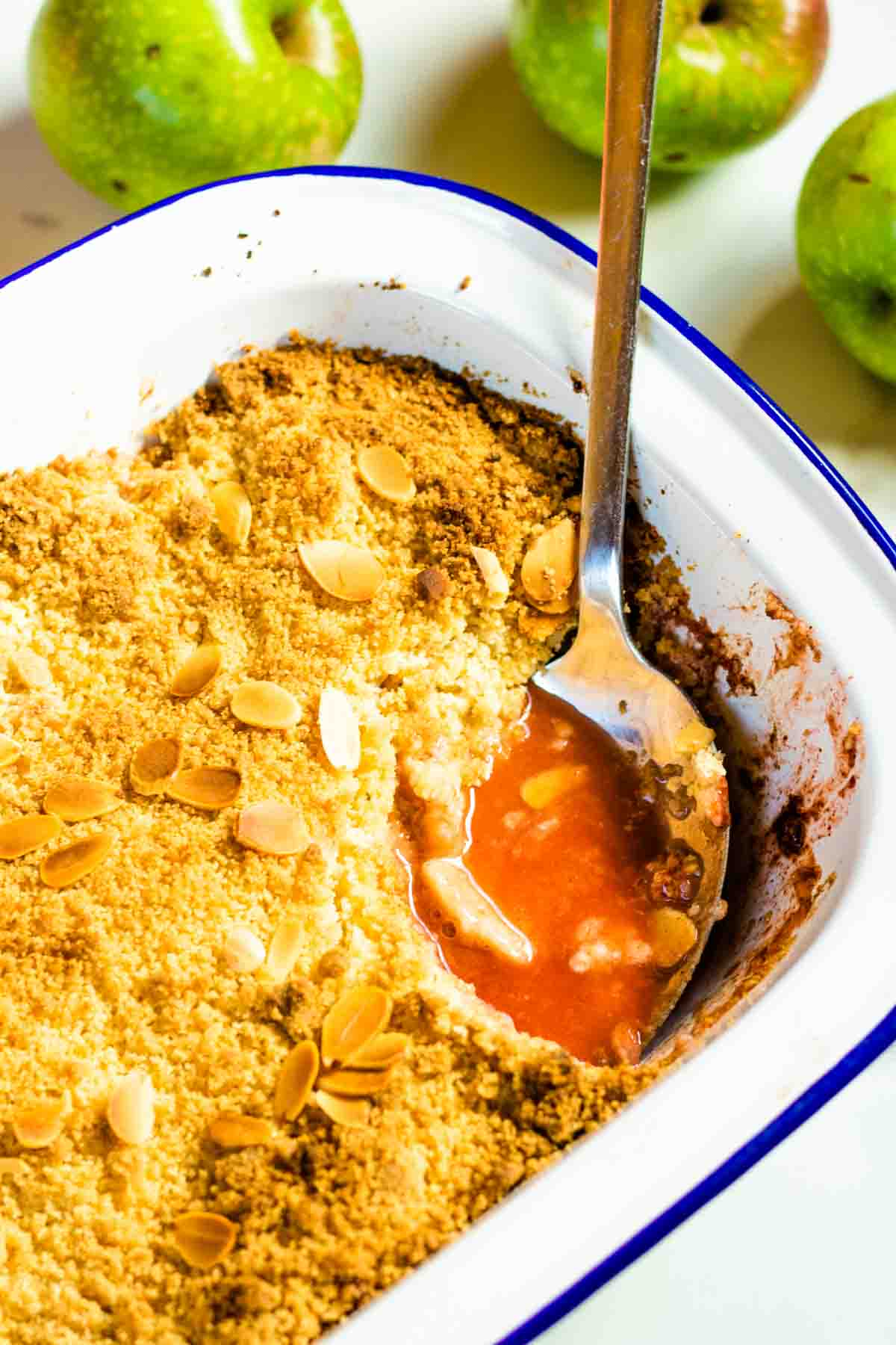 Large serving spoon dipped in strawberry juice of a homemade apple and berry crisp