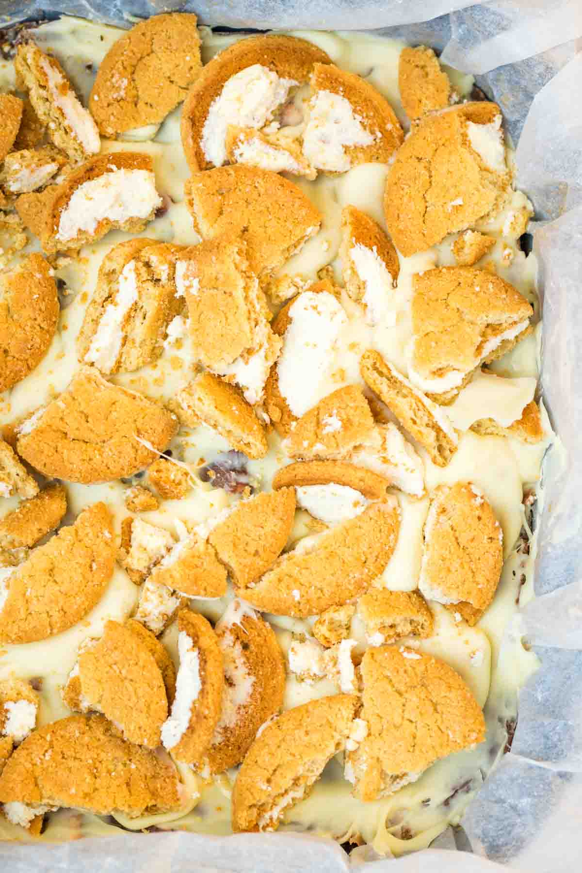 Close up of easy rocky road topped with white chocolate and broken Ginger creams in baking paper