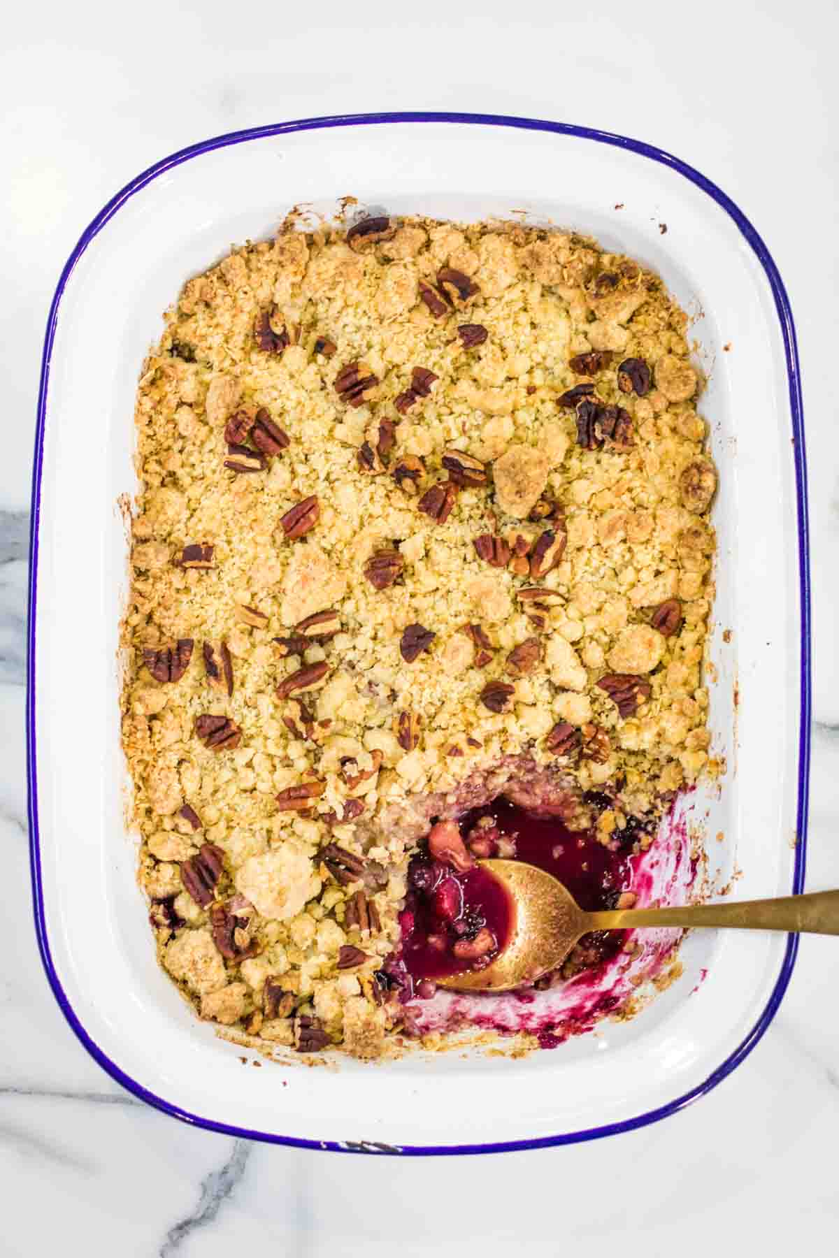 Pear crumble tart in a large white baking dish topped with toasted pecans with a spoonful missing