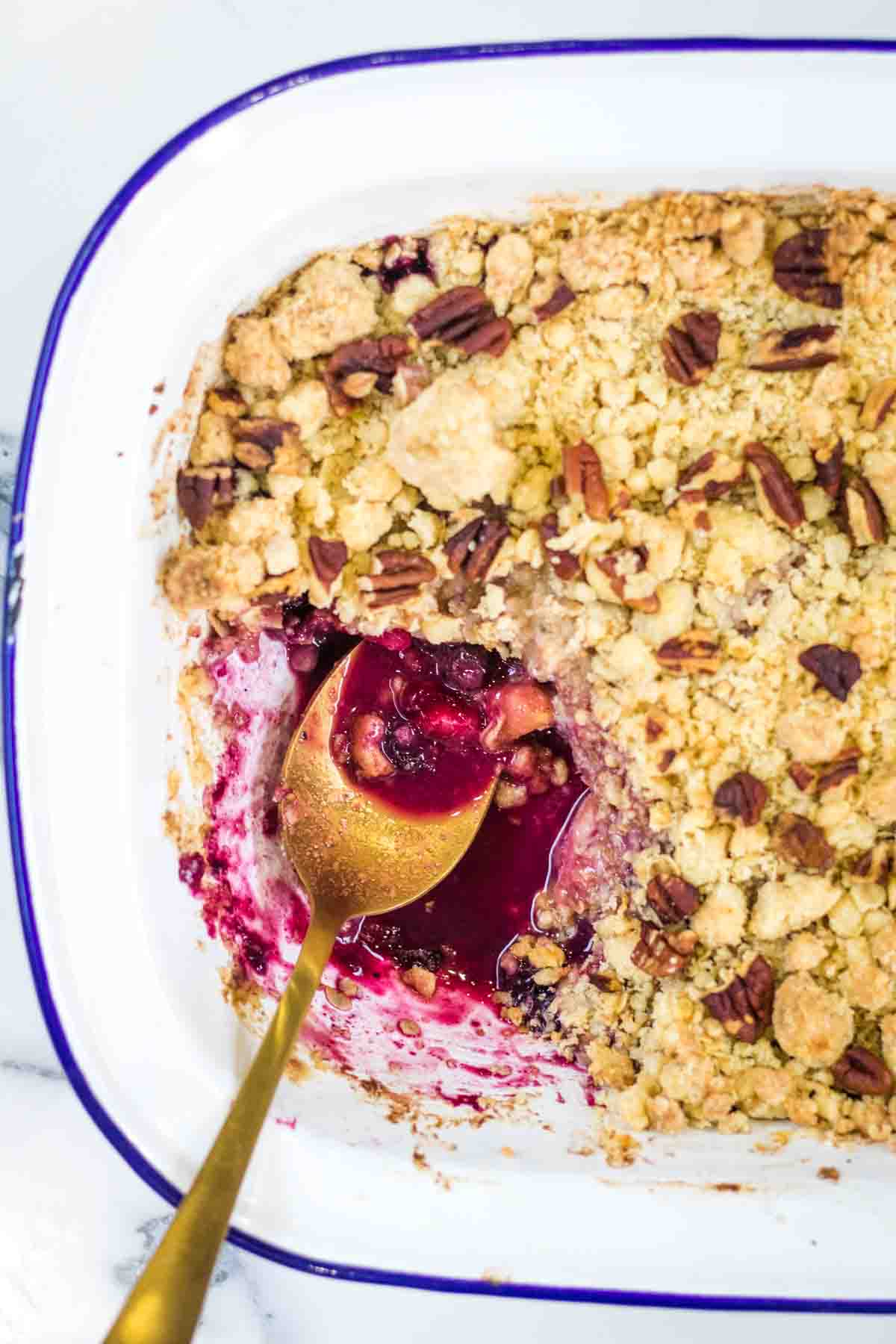 Close up of sweet cinnamon pear and blueberry syrup and gold spoon at the bottom of a baking dish.