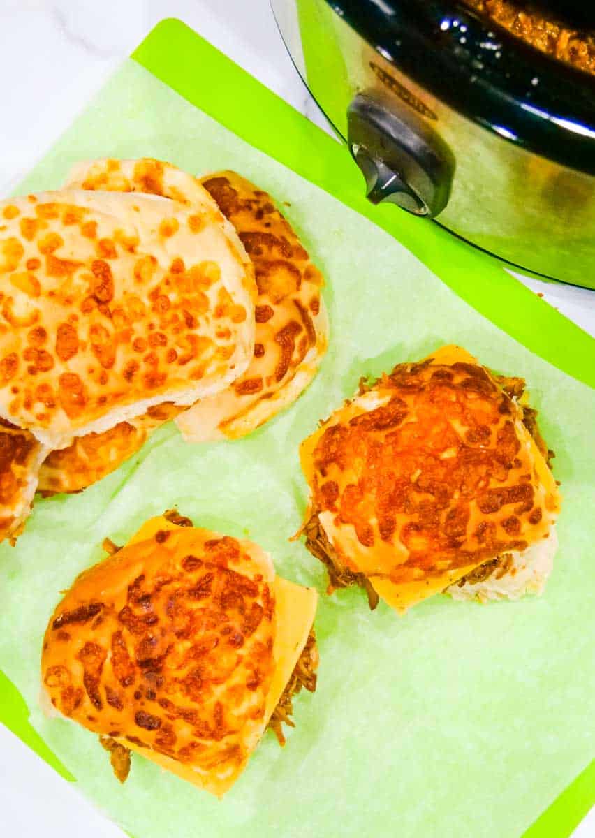 Cheese top hamburger rolls in front of a slow cooker with shredded BBQ pork