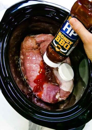 BBQ sauce being poured on top of pork in slow cooker