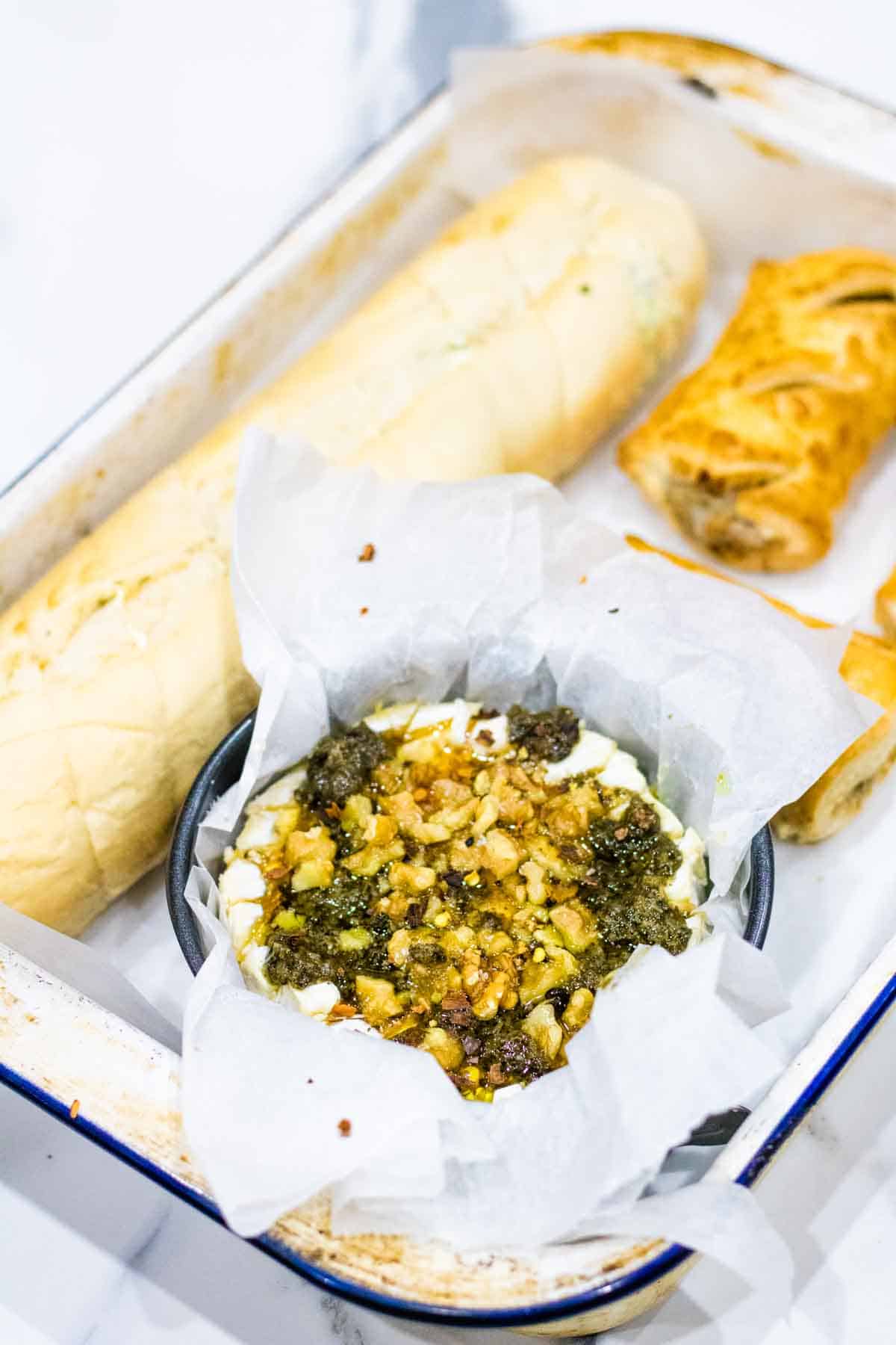 Camembert cheese on a baking tray with French baguette and sausage rolls before baking