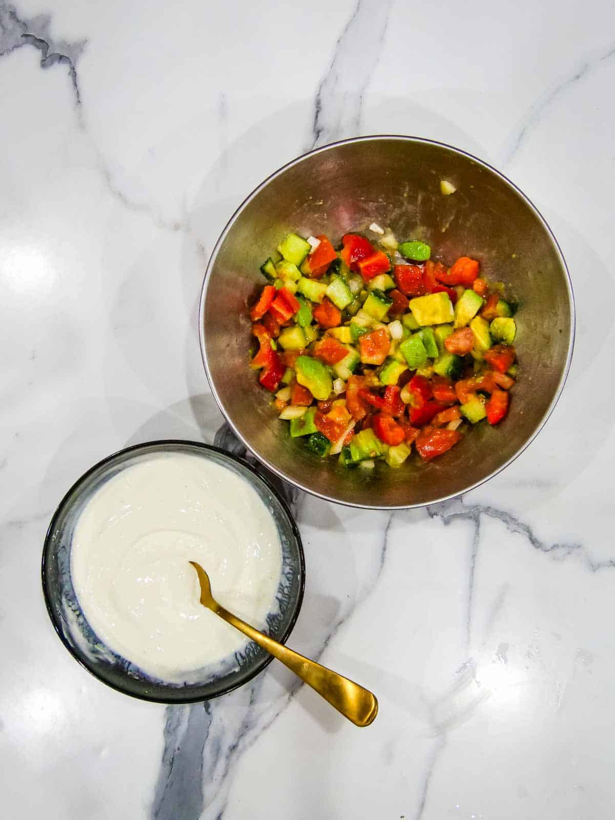 Lime sour cream in a bowl next to a bowl of salad on white marble kitchen counter