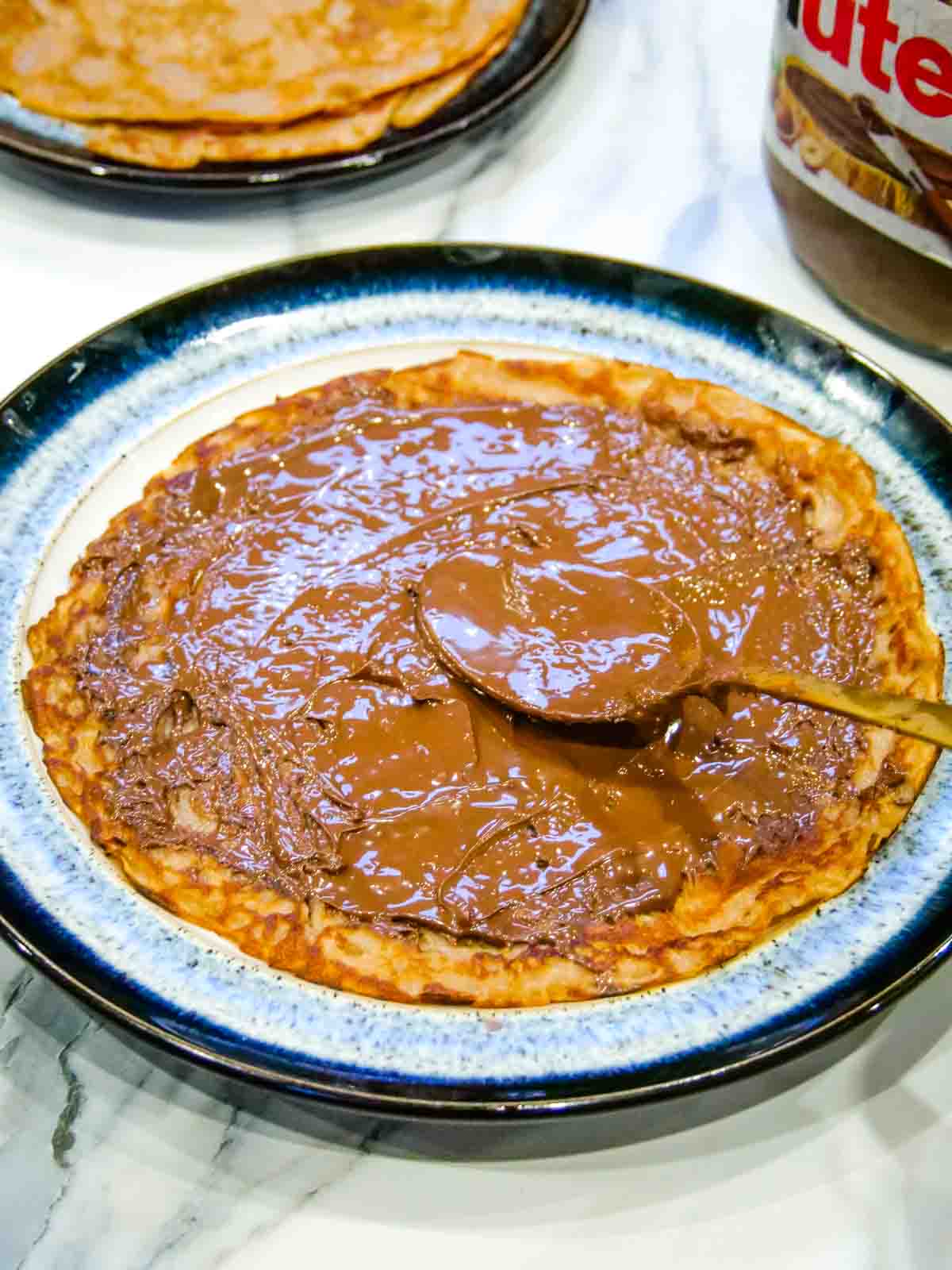 Spooning Nutella chocolate hazelnut spread on to chocolate pancakes