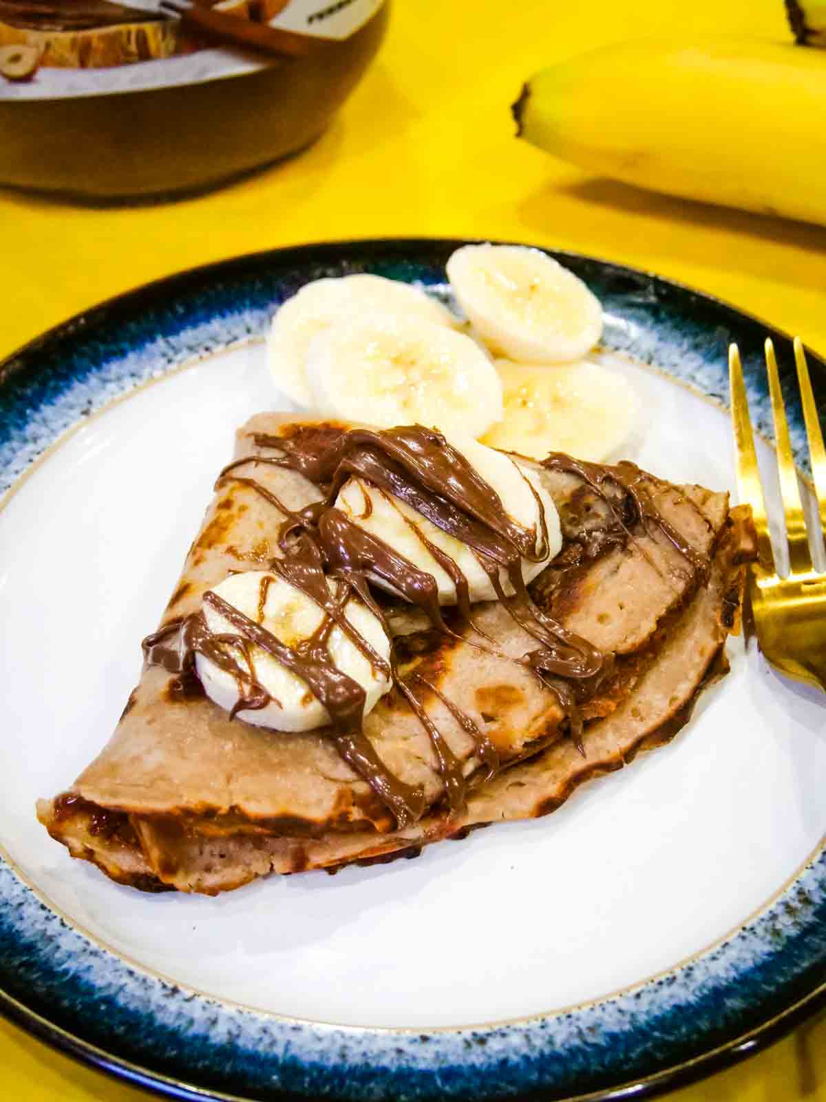Close up of banana topped crepe pancakes with banana and chocolate drizzled on a plate