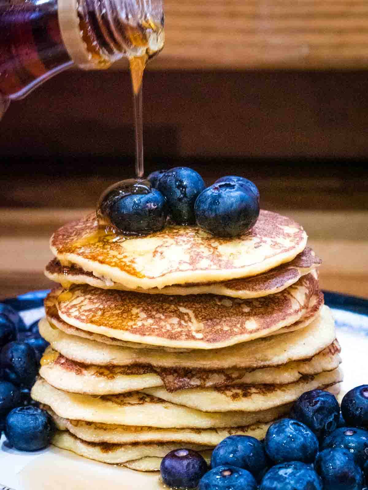 maple syrups being poured on a stack of pancakes with blueberries
