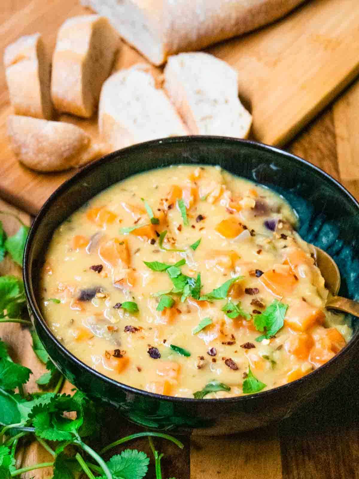 Close up of chunky lentil soup with sliced crusty bread on a chopping board