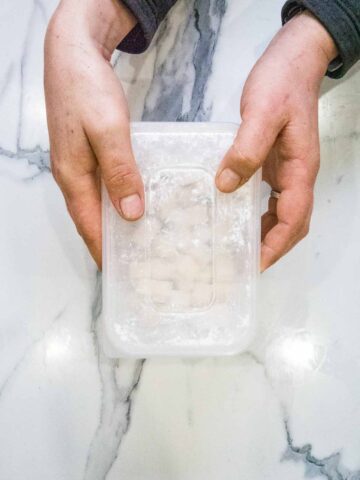 diced tofu in an airtight container with cornflour being shaken to coat everything well