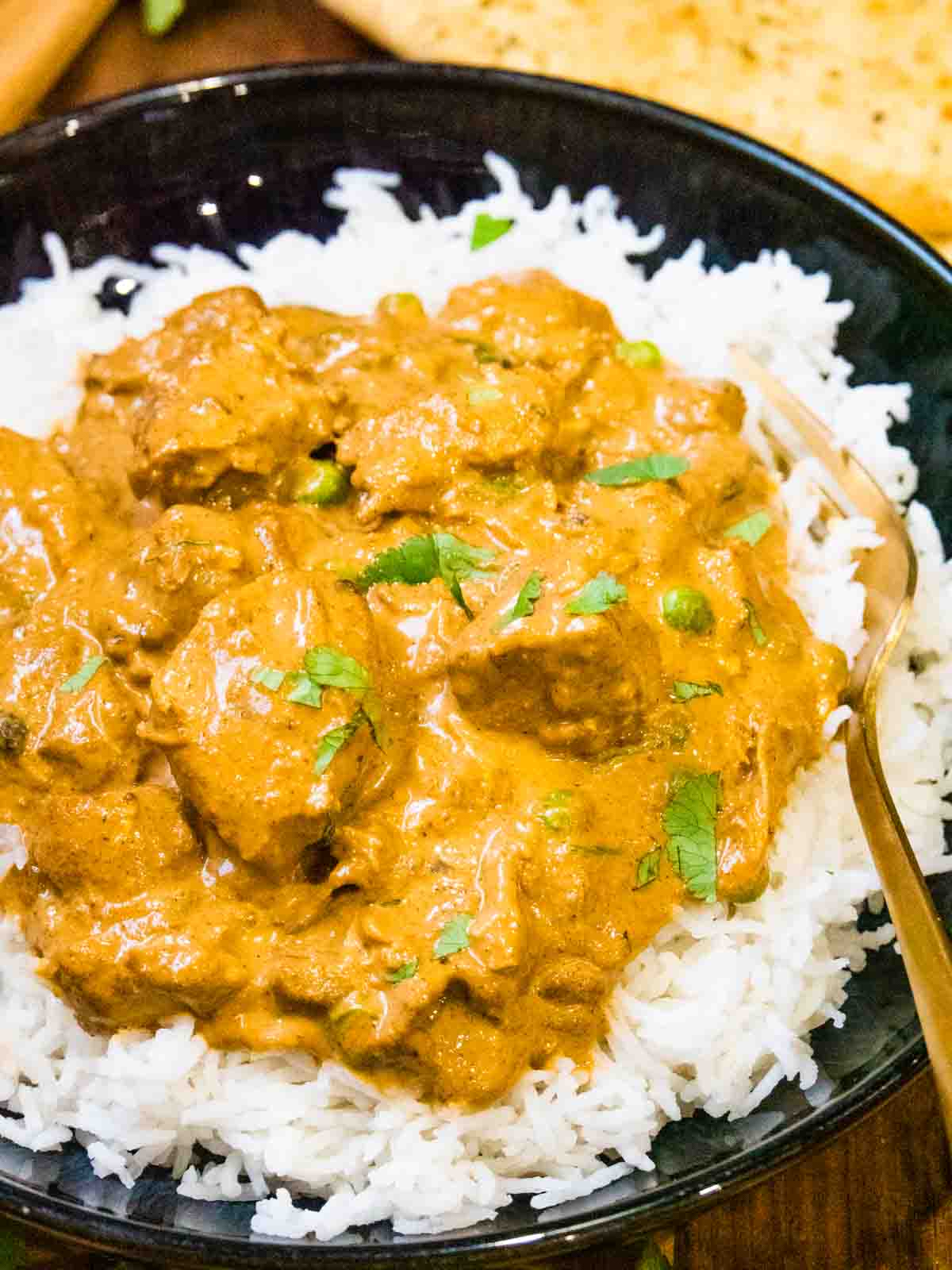 Chunks of chicken covered in curry sauce on rice with a gold fork and naan bread