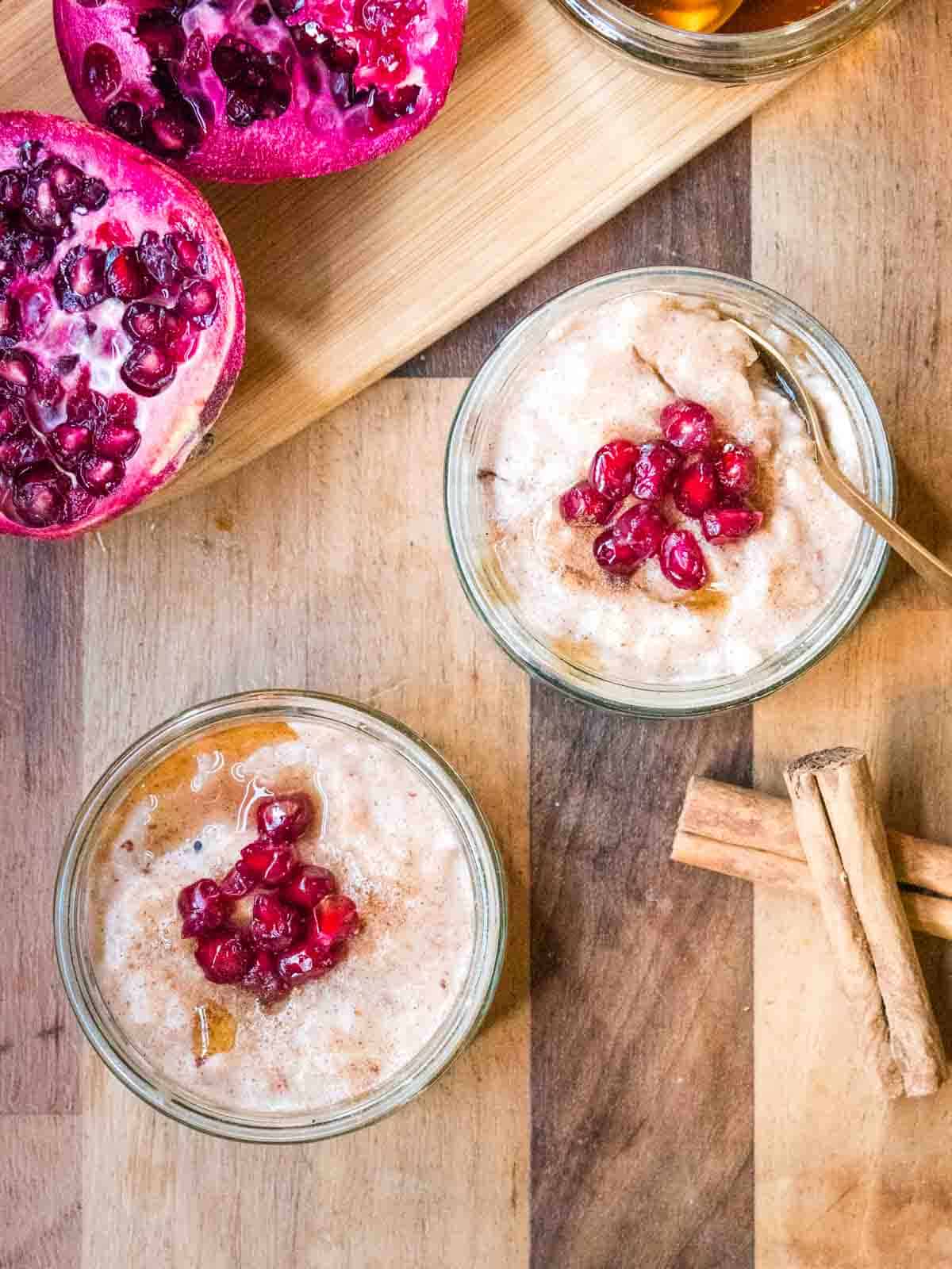 vegan rice pudding pots in GU pots topped with fruit, maple syrup and cinnamon sticks on the side