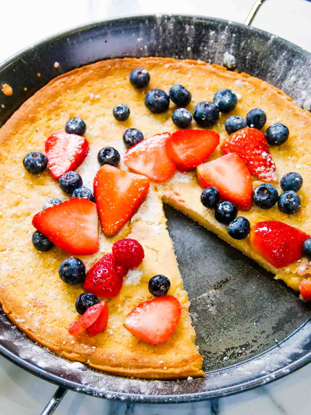 Giant pancake with strawberries and blueberries with a slice cut