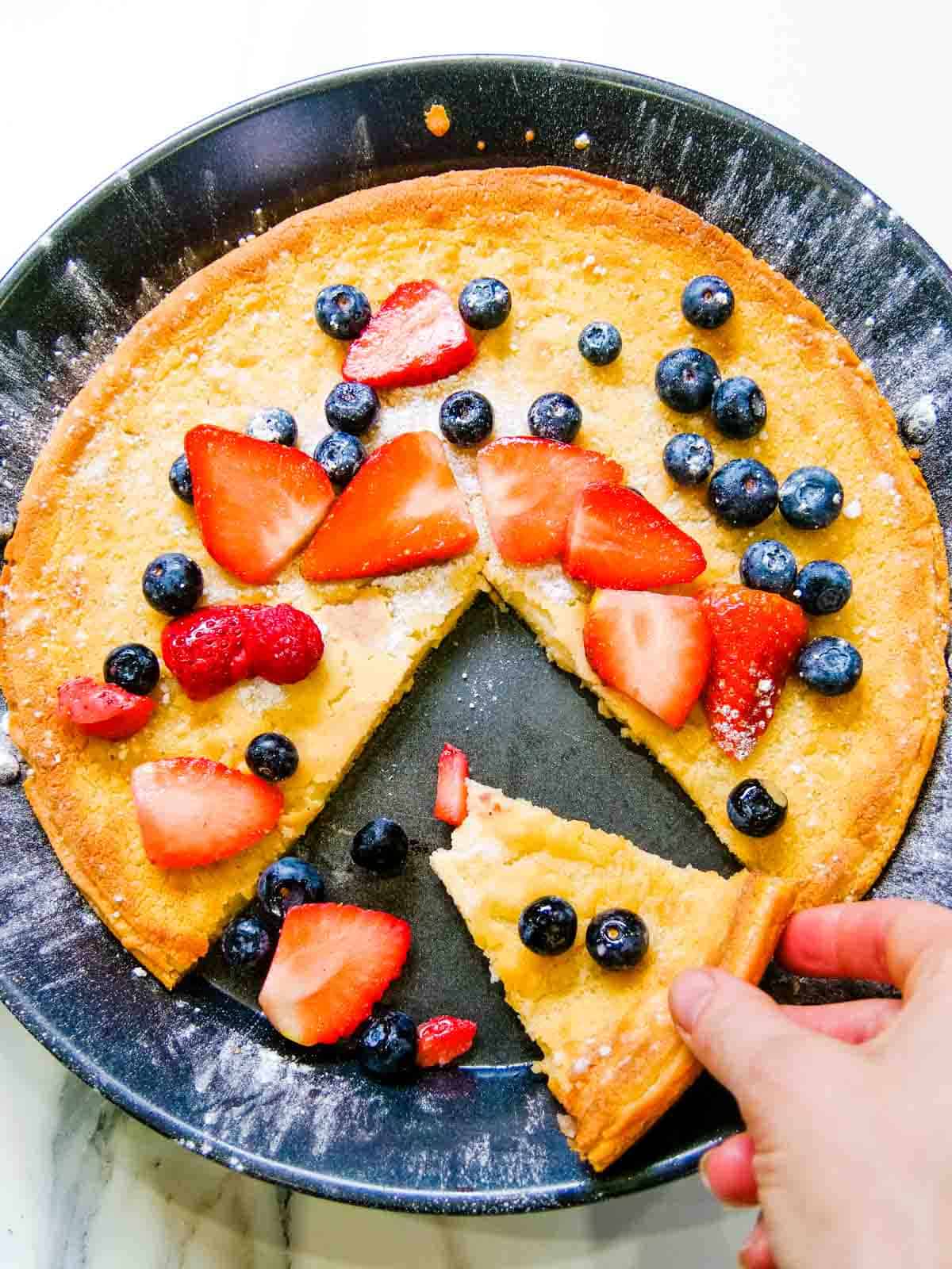 Person picking up a slice of a Dutch Baby pancake