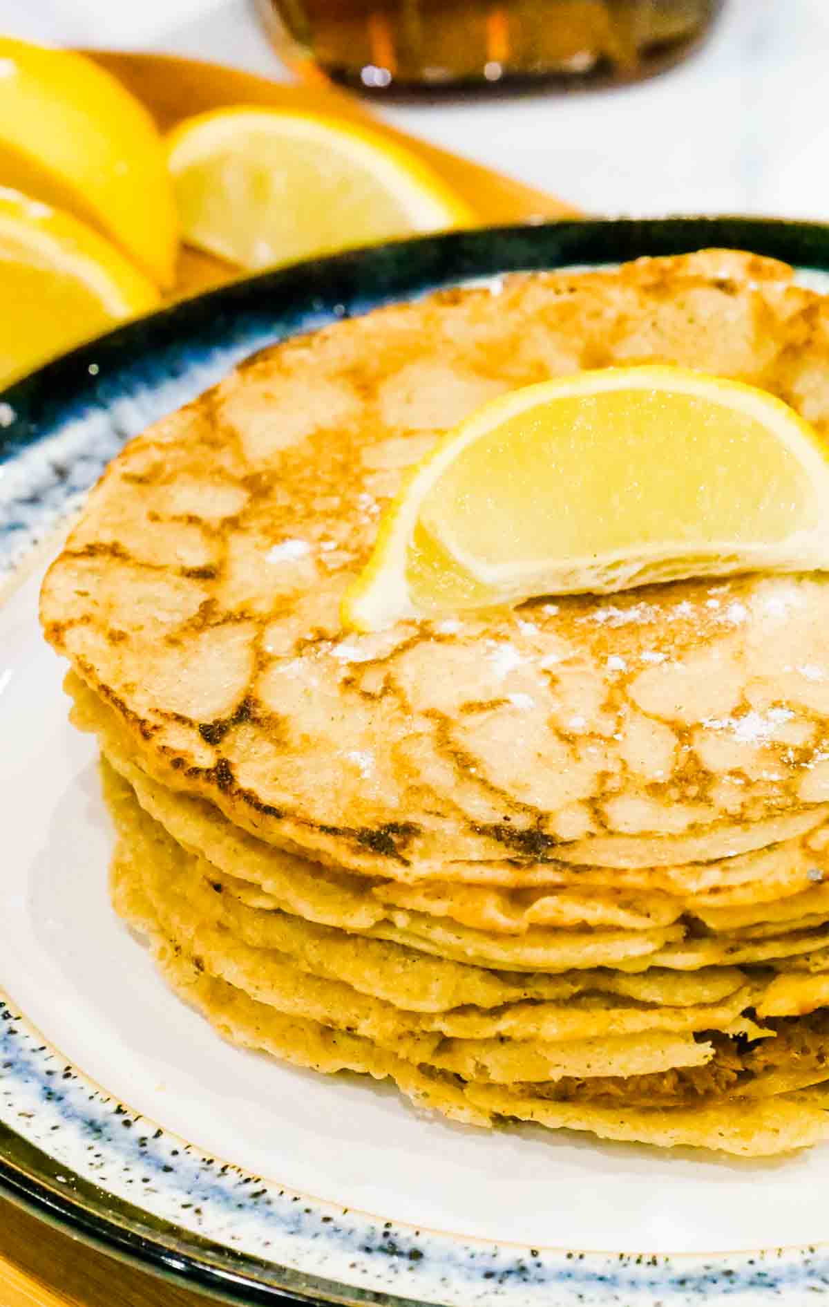 close up of a stack of pancakes with lemon wedge and icing sugar dusted on top