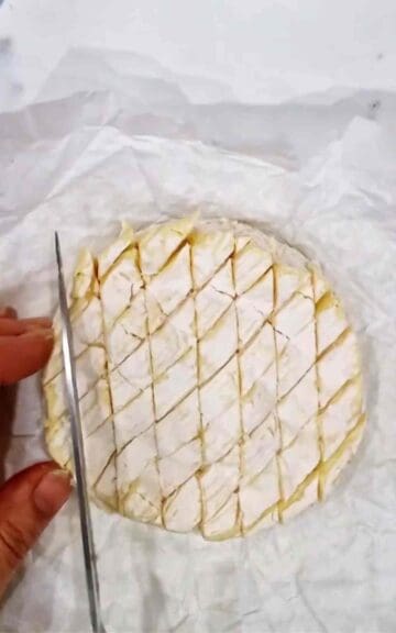 person scoring a criss cross pattern on top of raw camembert cheese round
