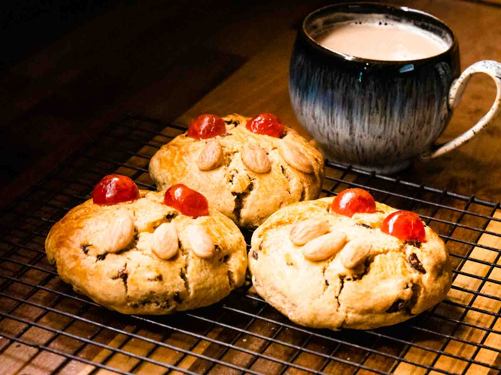Close up of some Yorkshire fat rascals with cherries for eyes and almonds for teeth on a wire rack and a cup of tea