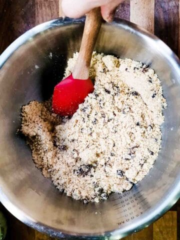 person mixing in spices, sugar, citrus peel and dried fruit in a large mixing bowl
