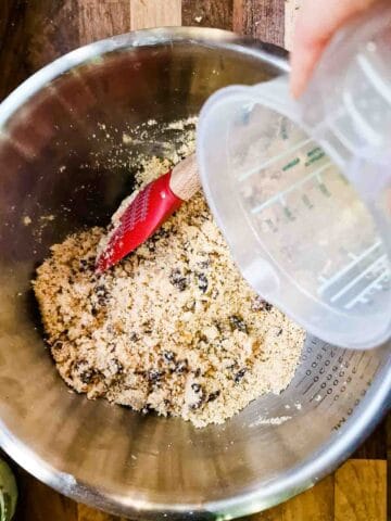 person pouring beat egg into a large mixing bowl to bind the fat rascal cake mixture