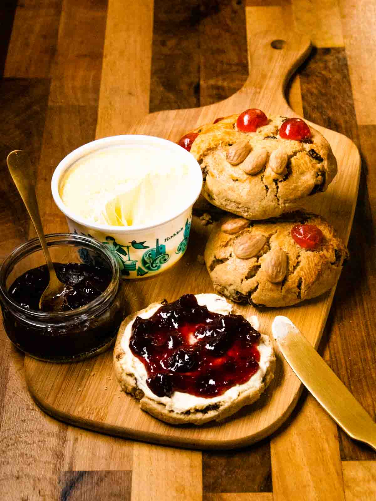 clotted cream and jam being spread on a sliced Fat Rascal on a bamboo serving platter