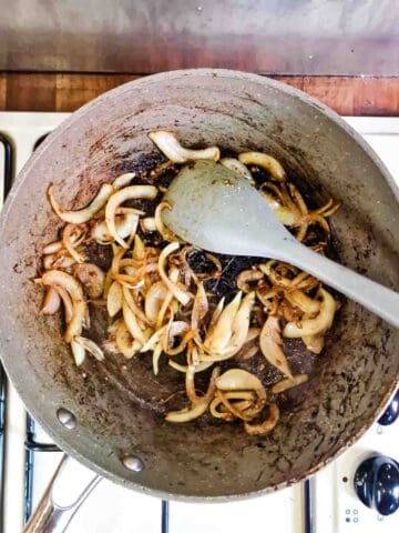 fried onions and garlic in a frying pan on the hob with grey silicone spatula